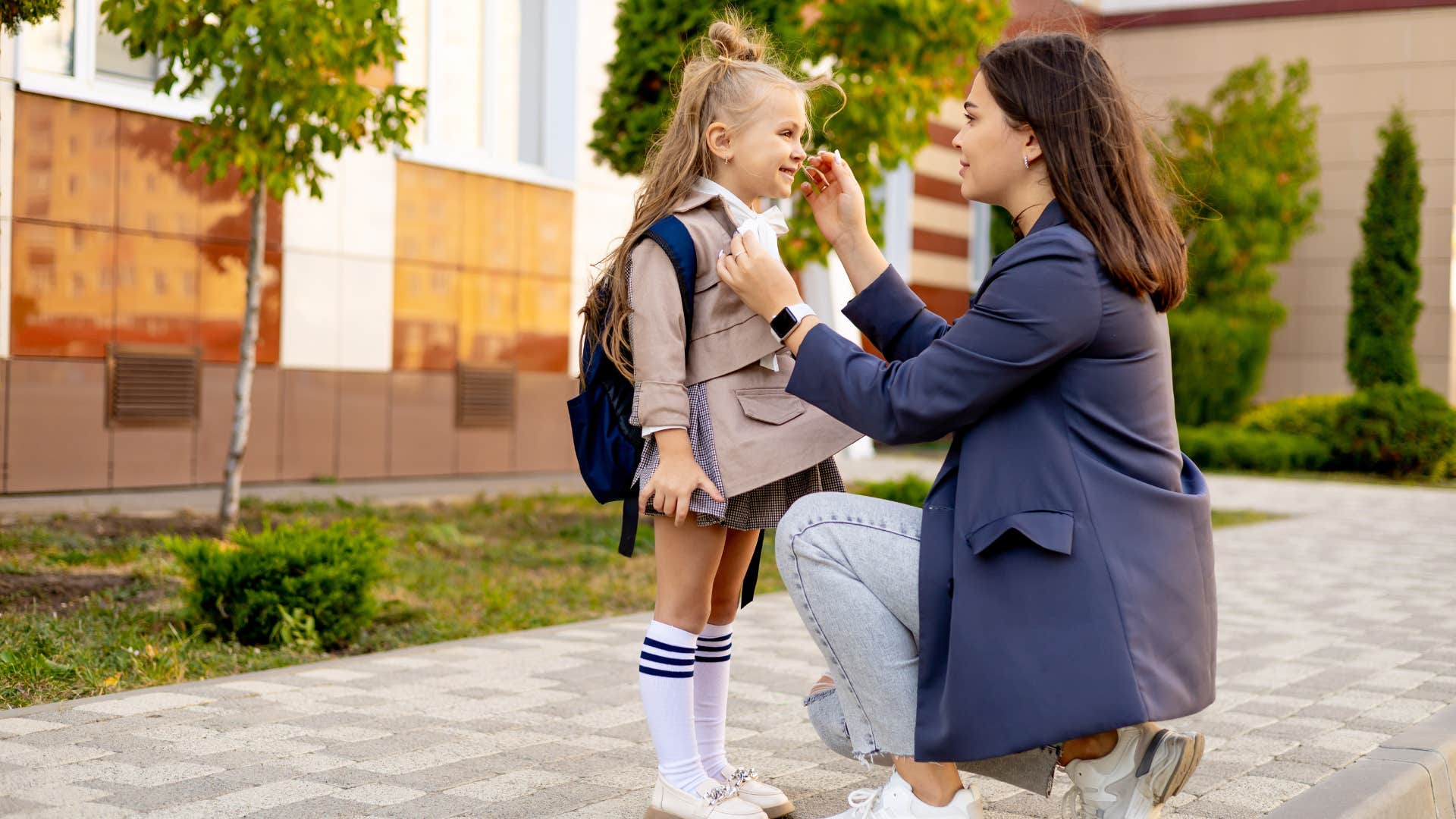 mom kneeling while talking to child in uniform