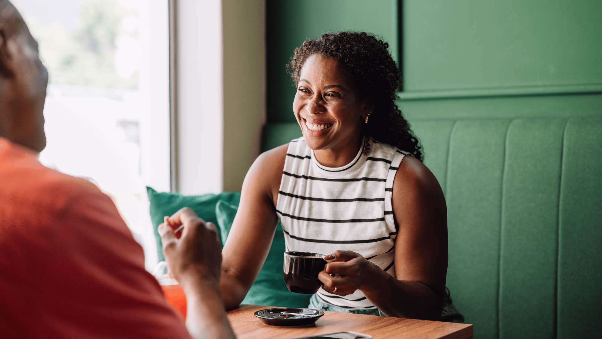 woman smiling while having coffee in a booth