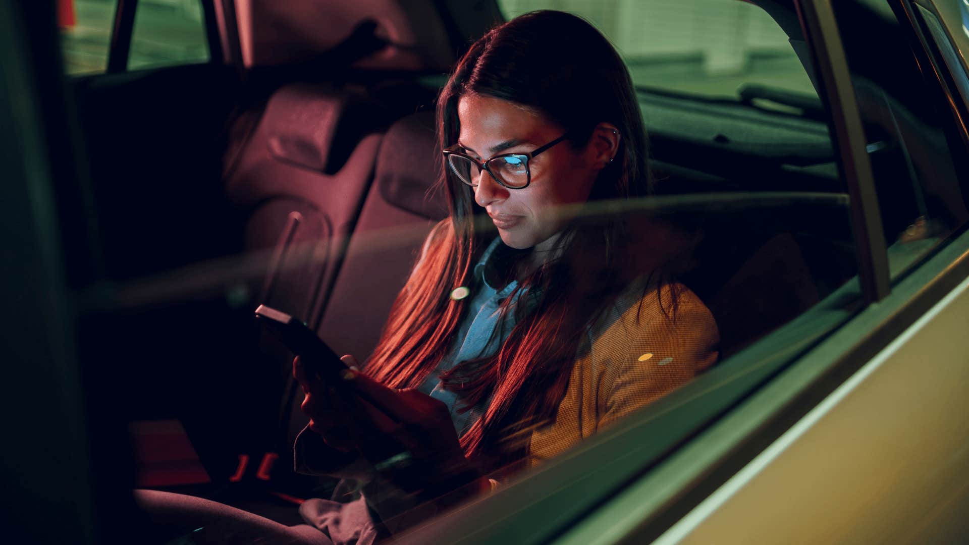 woman texting on phone while in a taxi