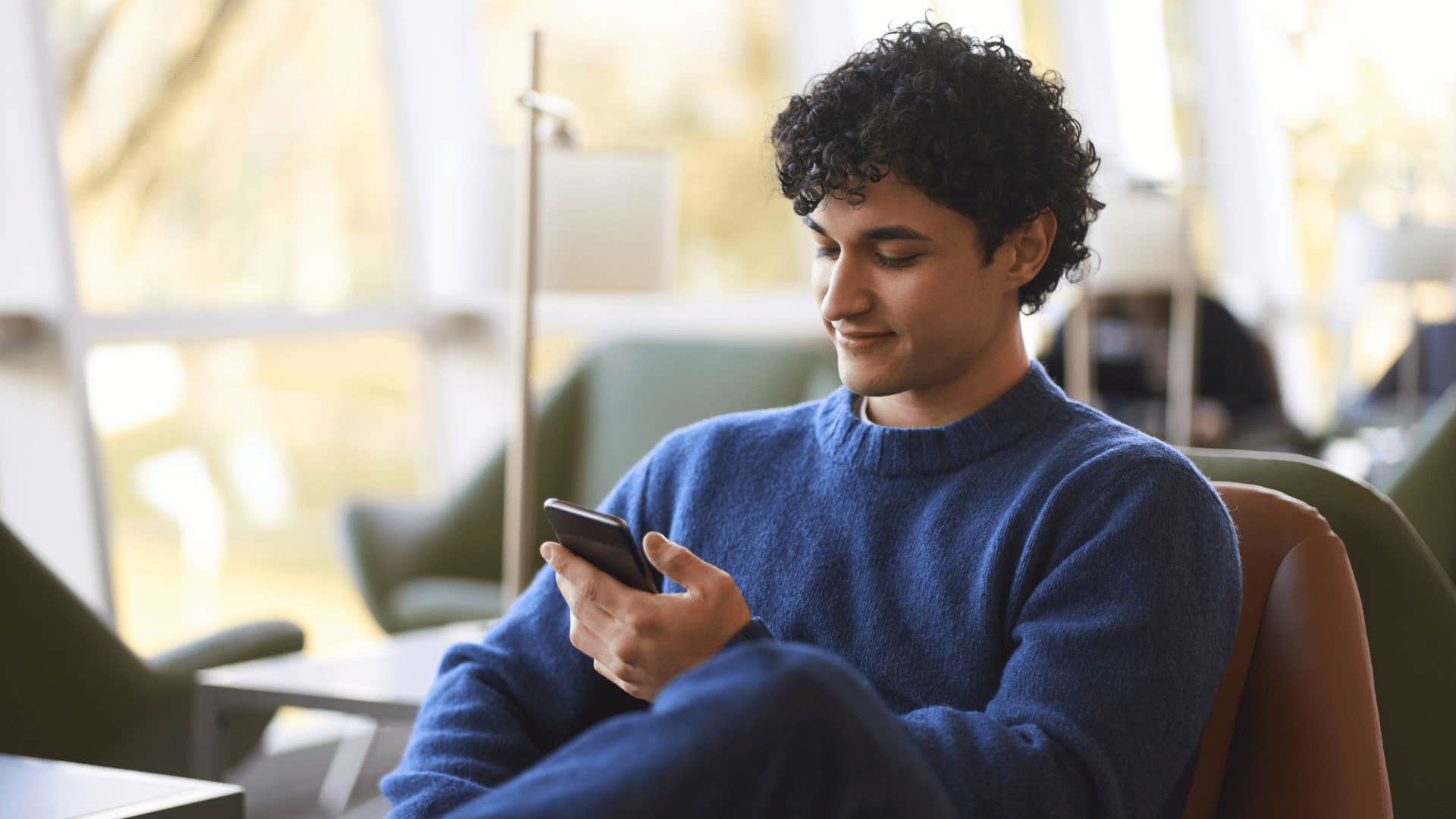 Gen Z man looking at phone while sitting down