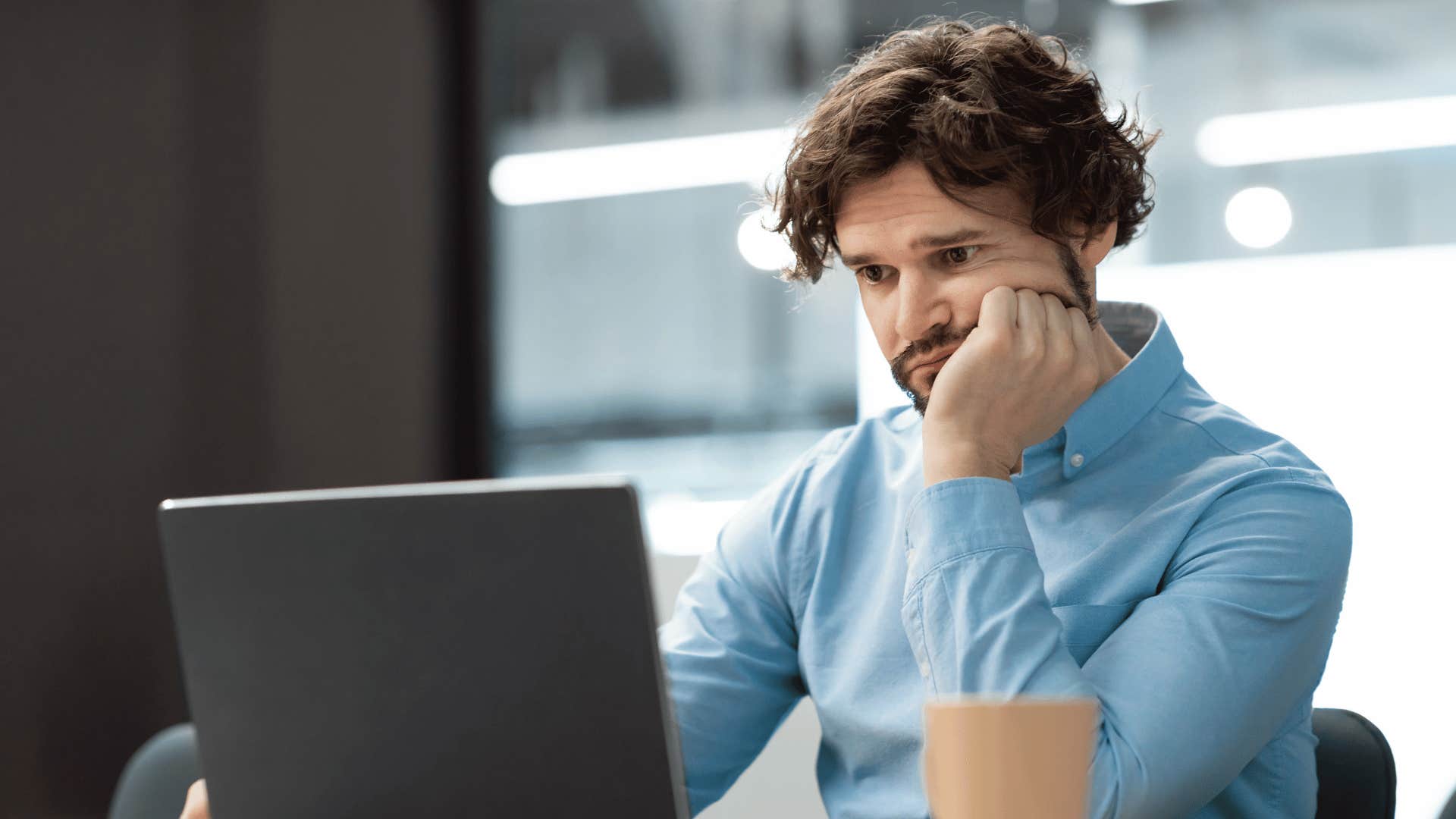 Gen Z man looking bored as he stars at laptop