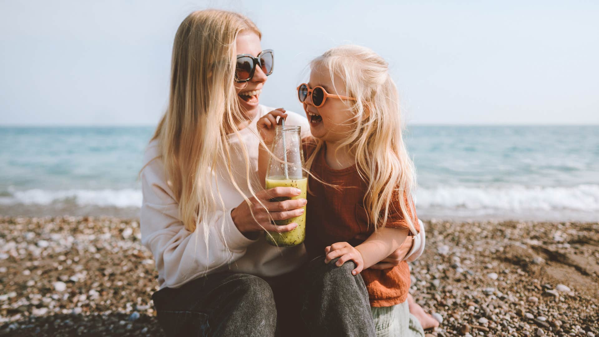 Family mother and daughter child drinking smoothie on beach 