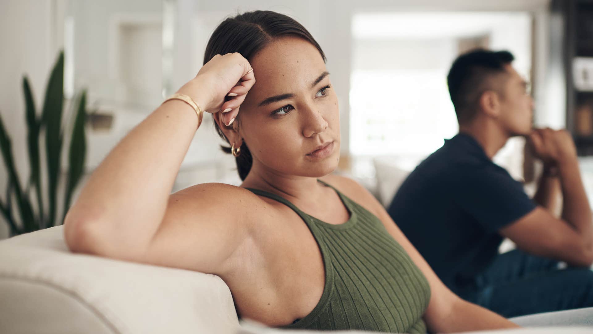 upset woman sitting on edge of couch away from husband