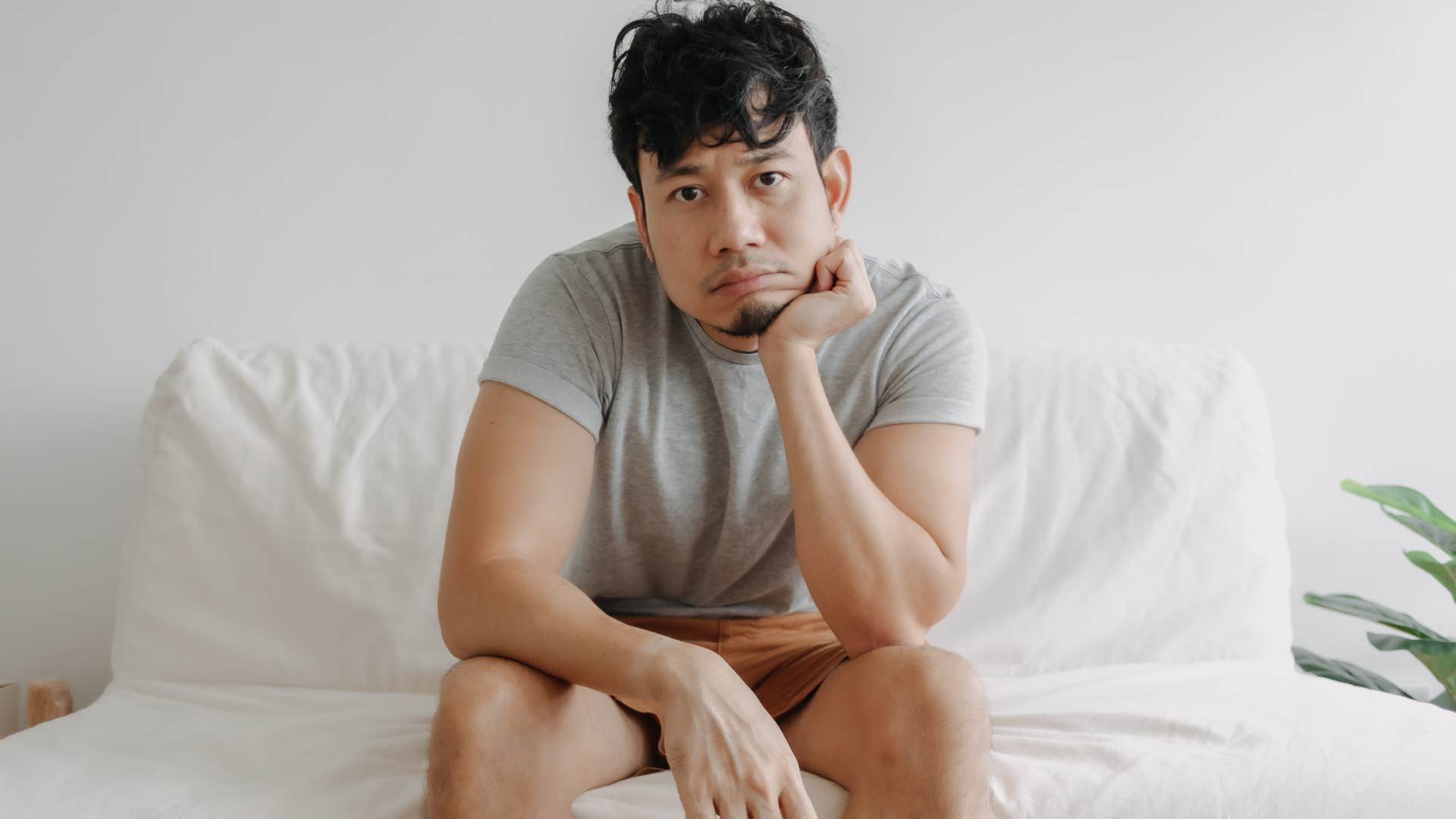 portrait of lonely man sitting on bed at home staring at camera