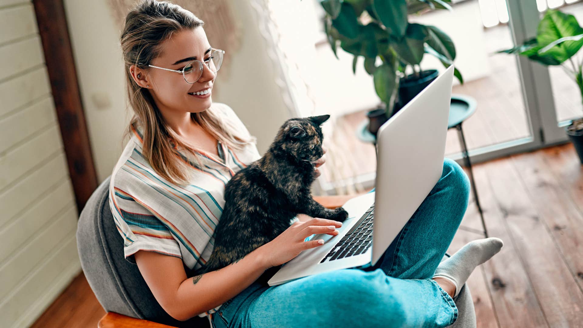 young woman in glasses working on a laptop with her cat