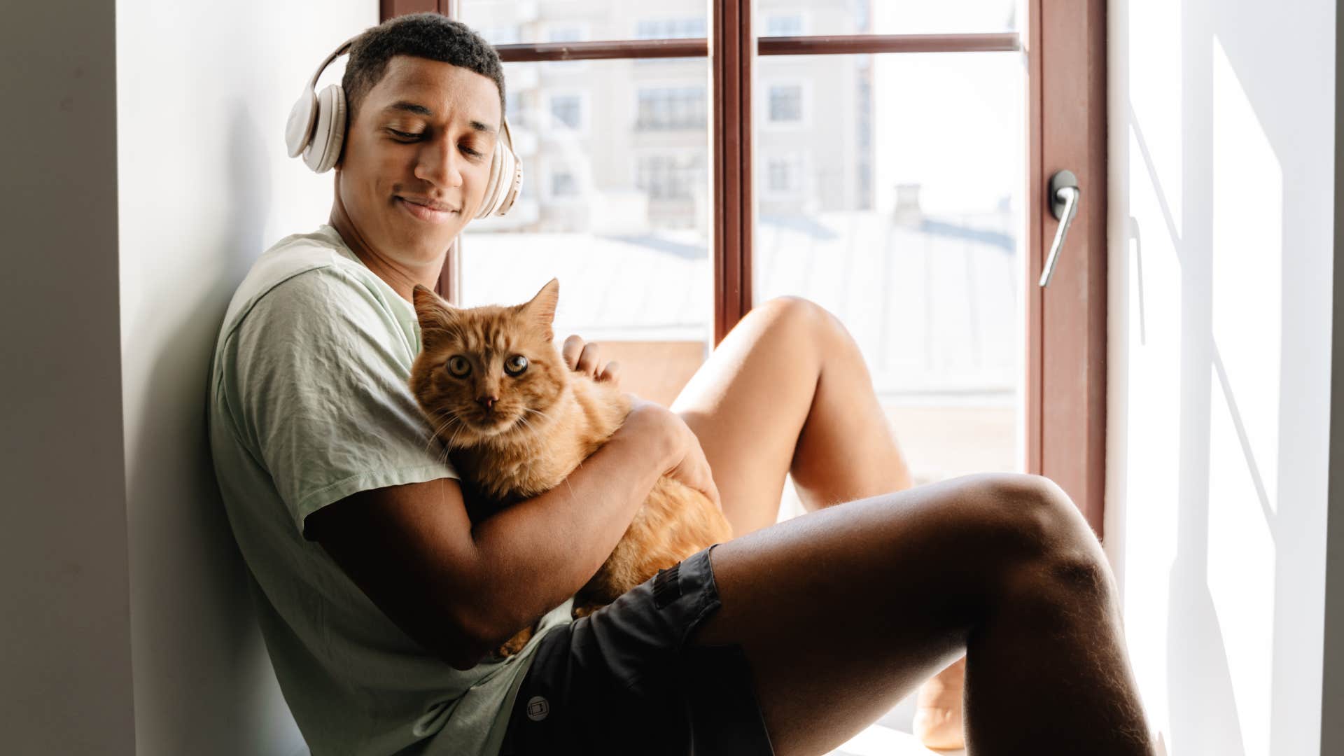 Black man in headphones sitting with his cat on windowsill