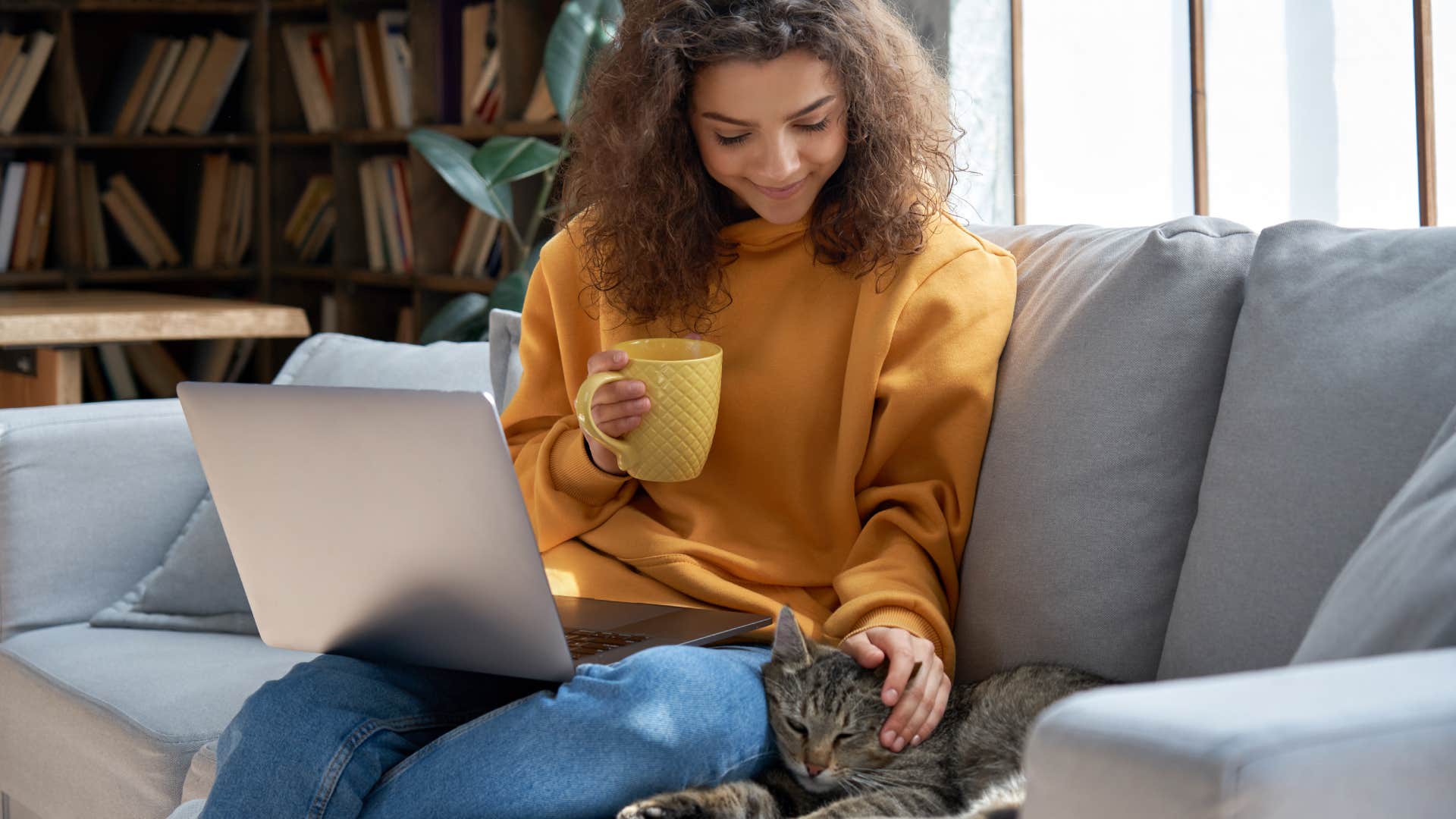 woman sitting on couch petting cat next to her