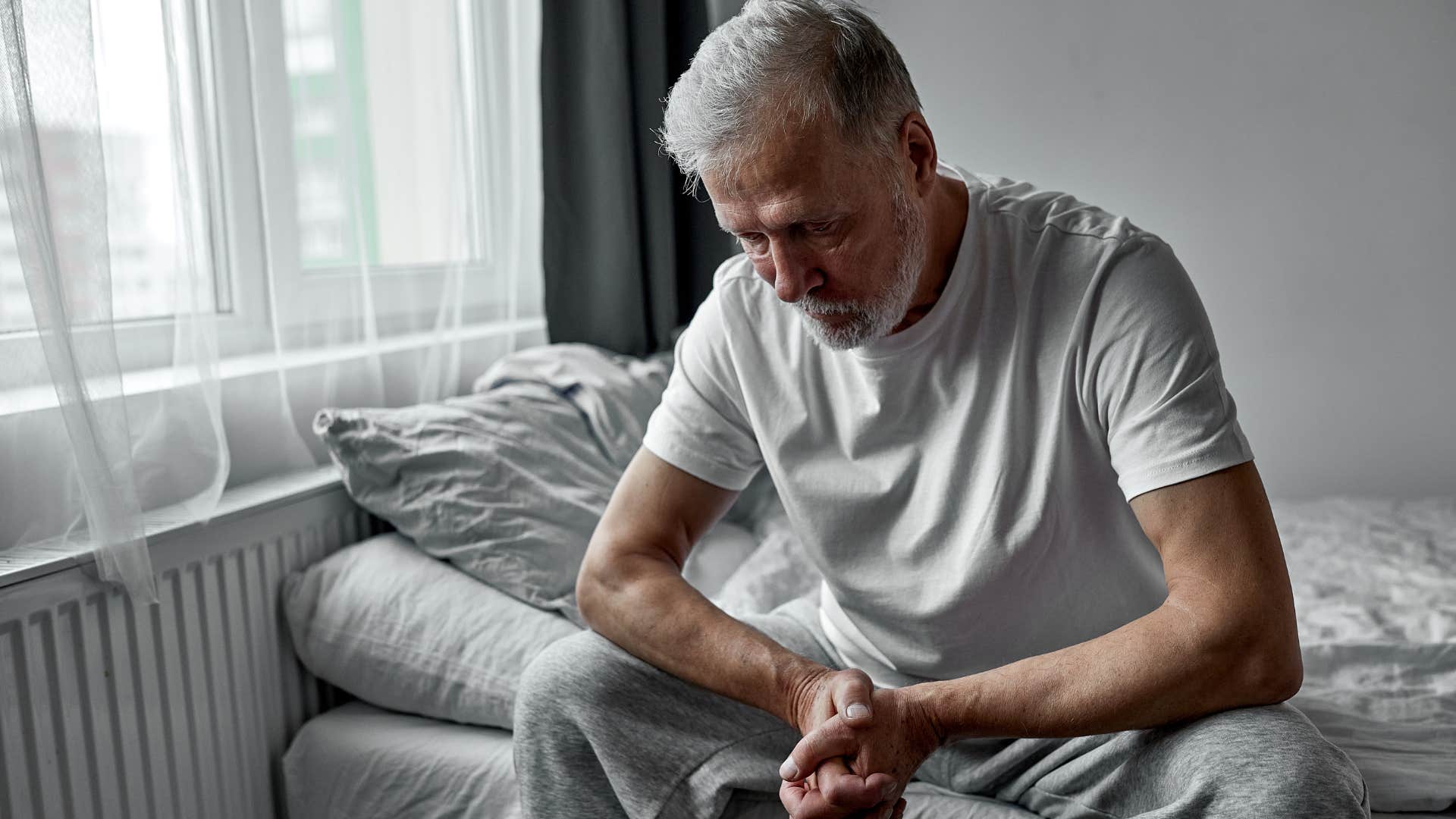 older tired man sitting in his bed