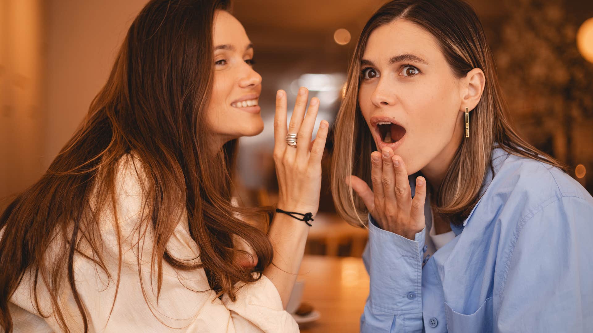 Two women gossiping with each other on a couch.