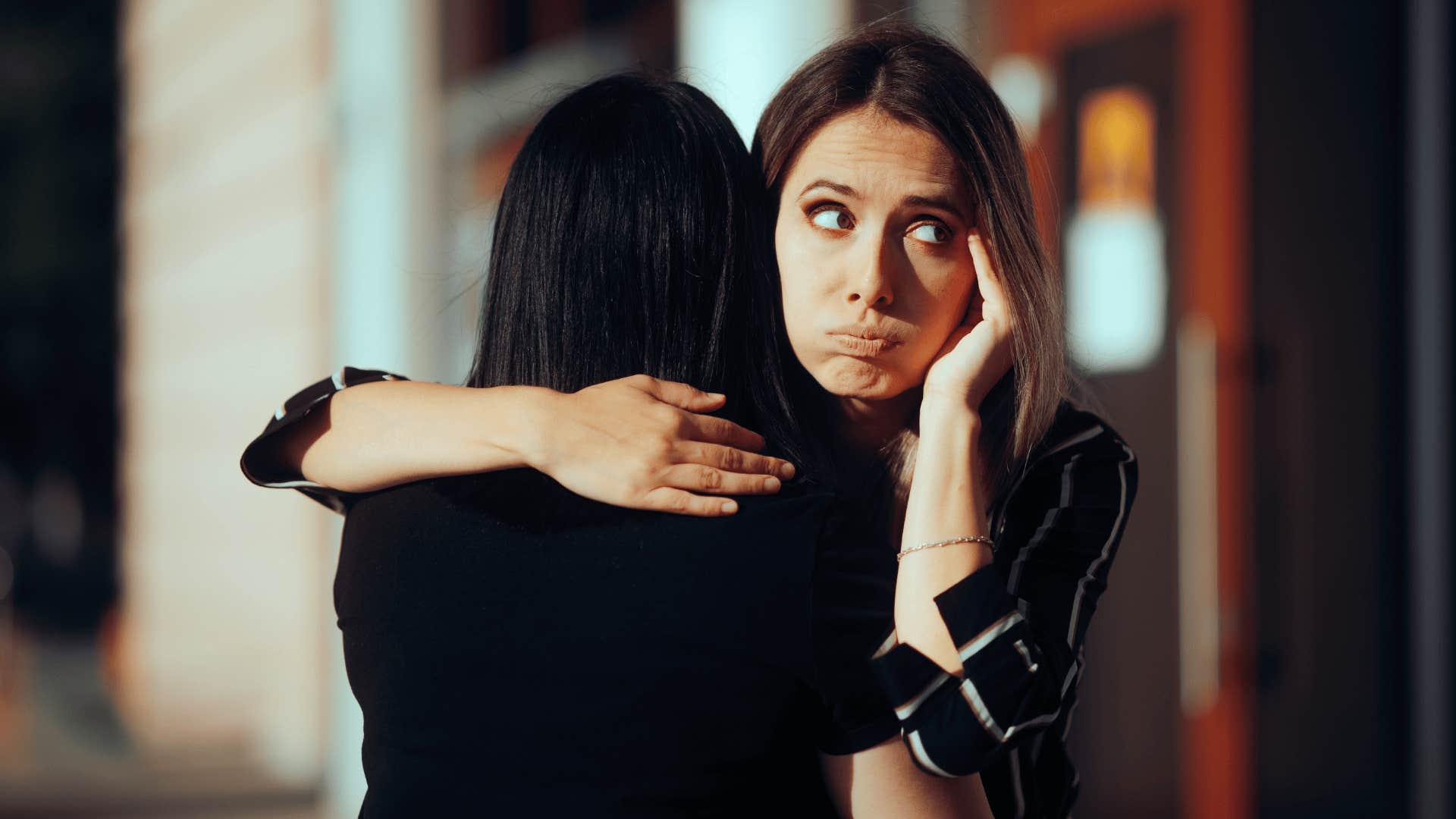 woman looking annoyed as she hugs friend