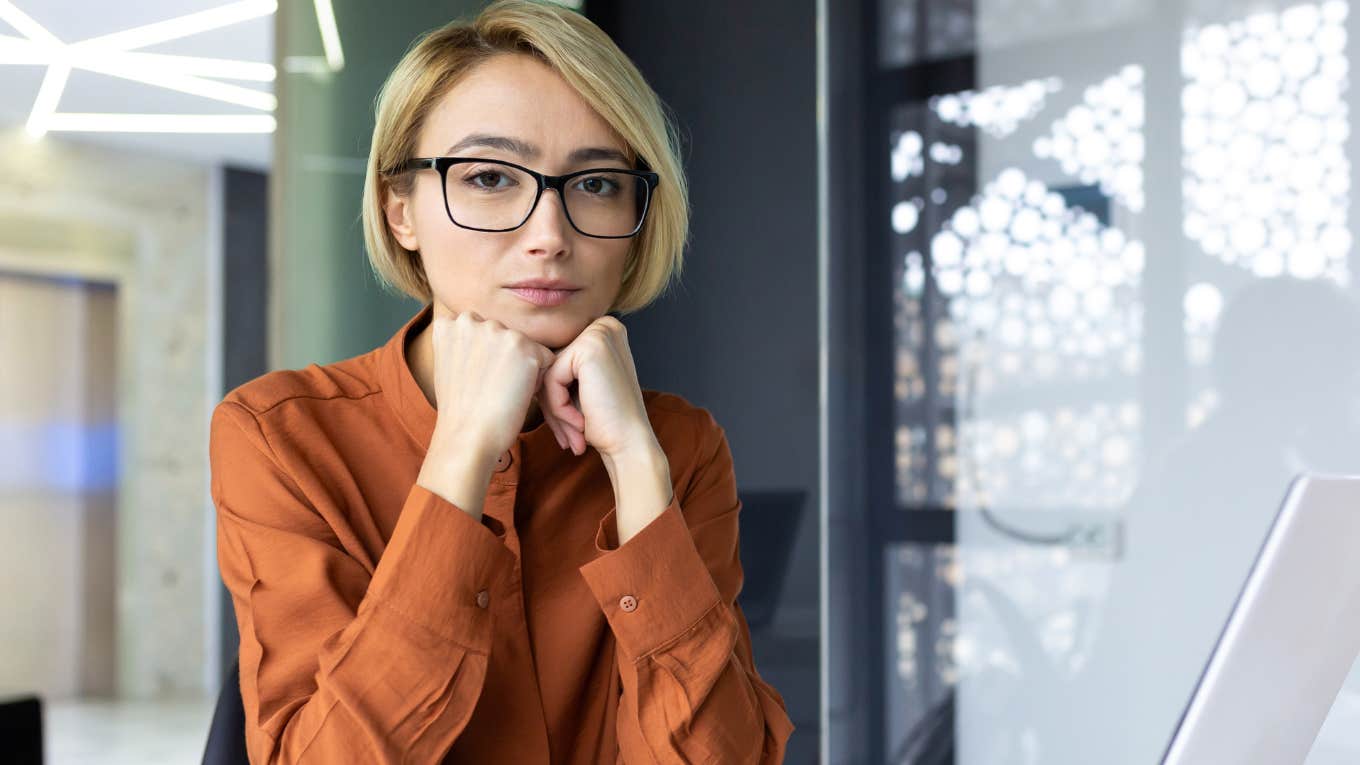 woman with hands under chin wearing glasses at work