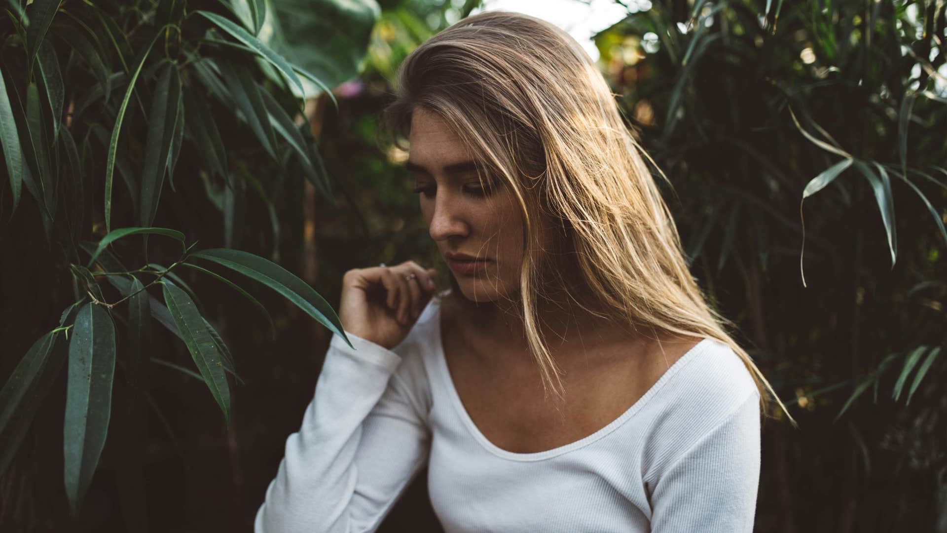 blonde woman with white shirt by a large green plant