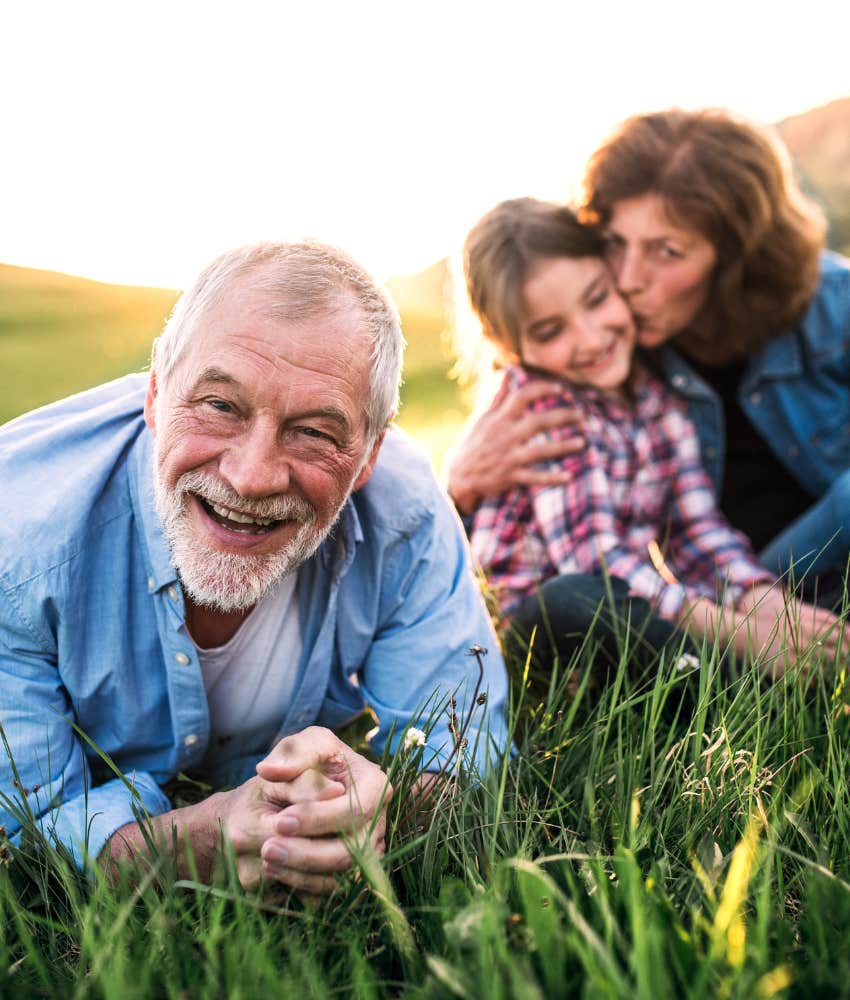 Senior couple with granddaughter outside in spring nature, relaxing on the grass.