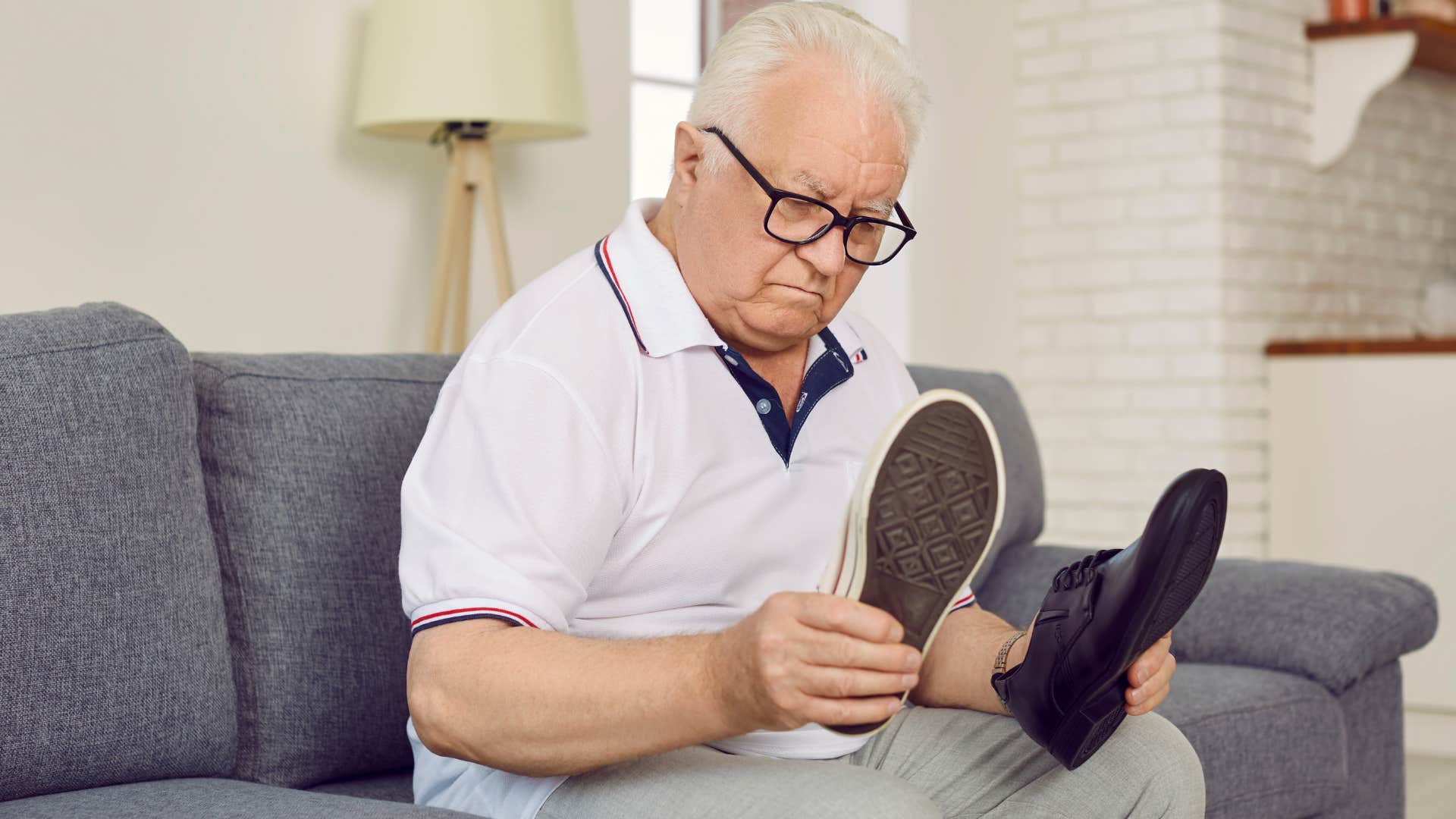 Boomer man looking at two pairs of shoes on his couch