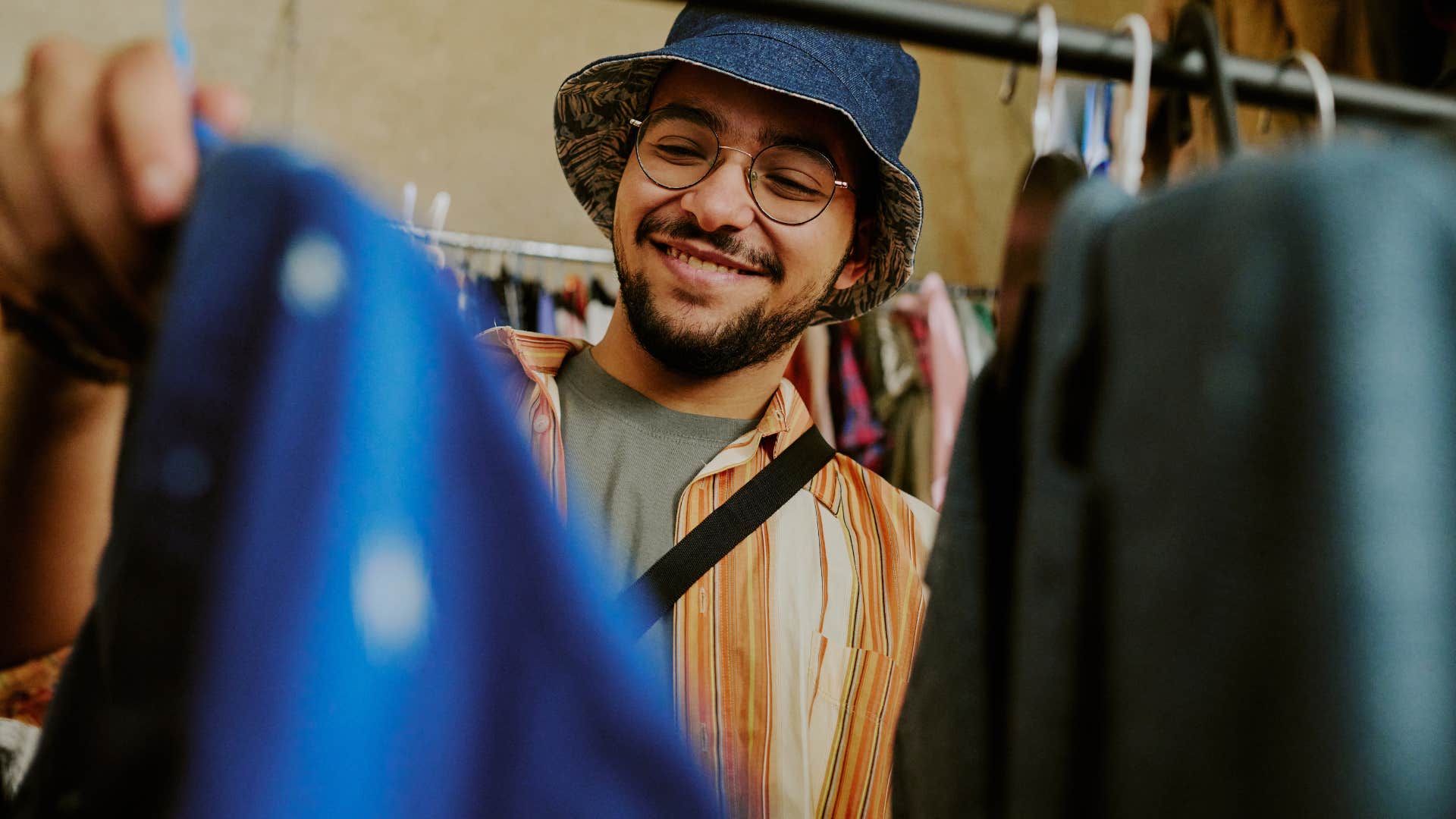 Gen Z man smiling and looking at clothes at thrift store