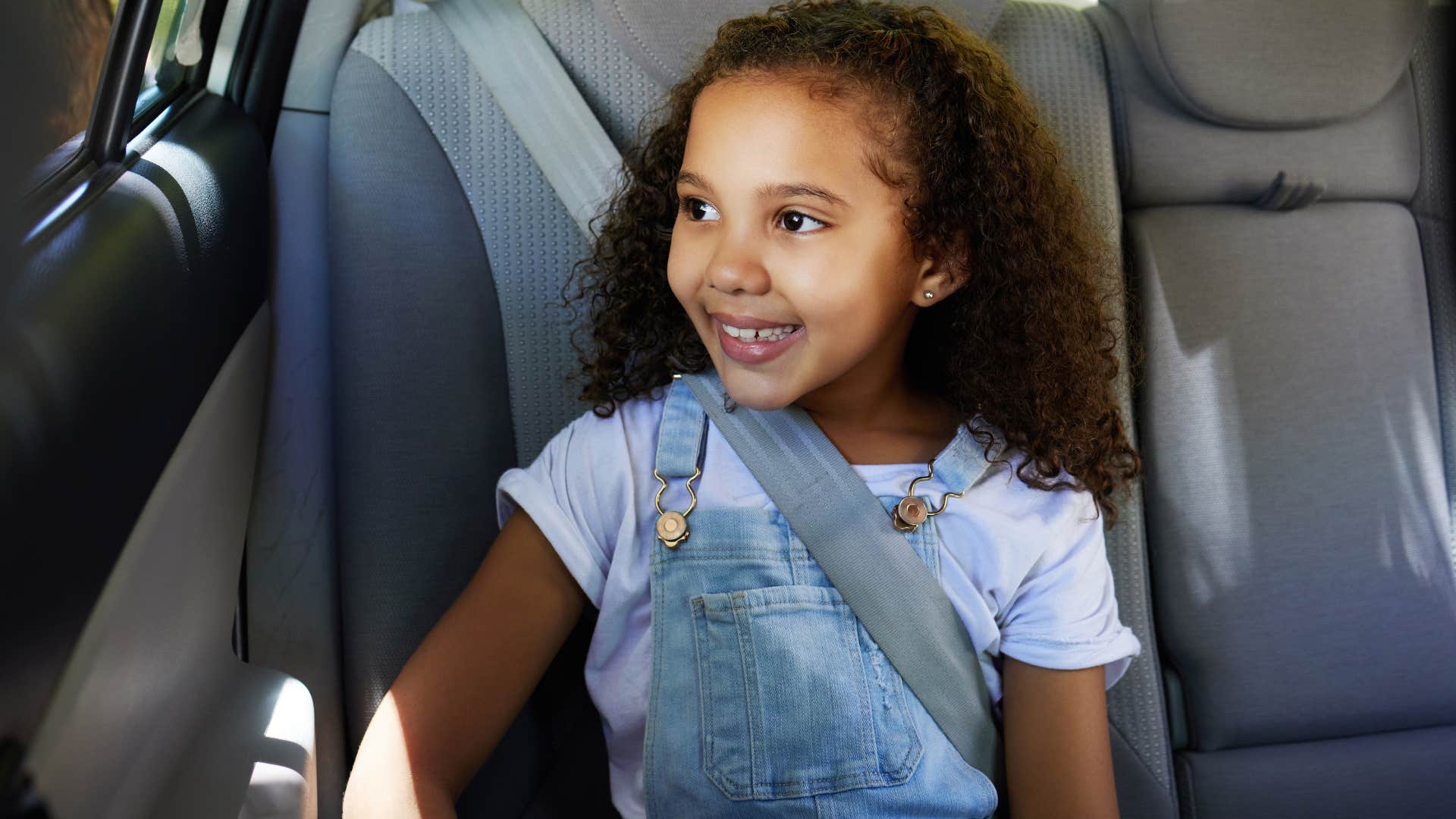 little girl smiling in the backseat of a car