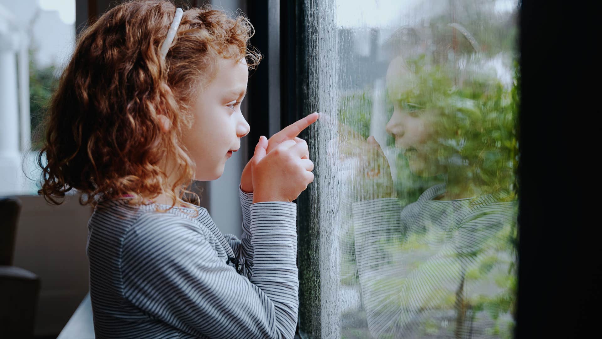 girl pointing at rain outside of a window