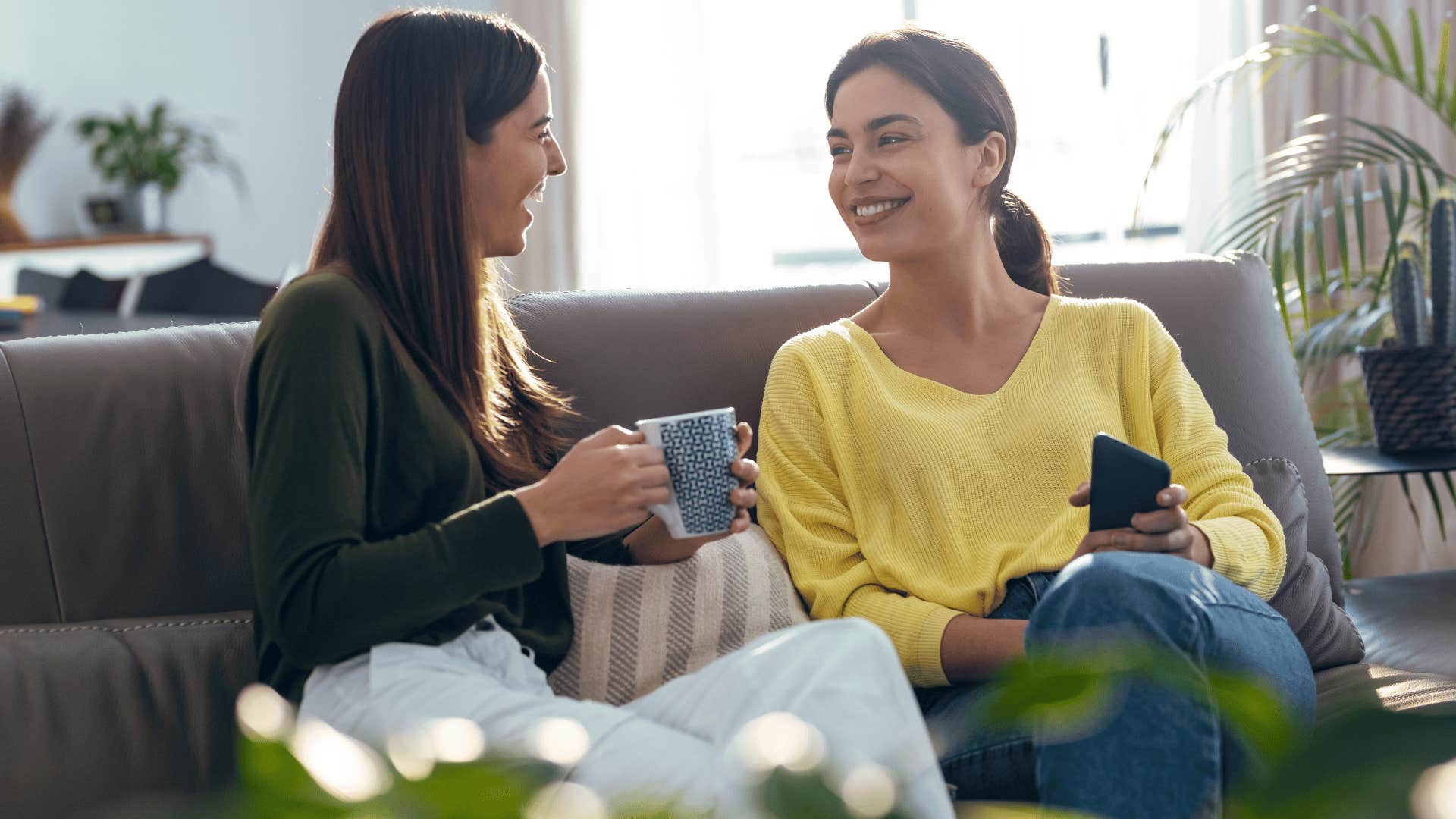 two women chatting on the couch while drinking coffee