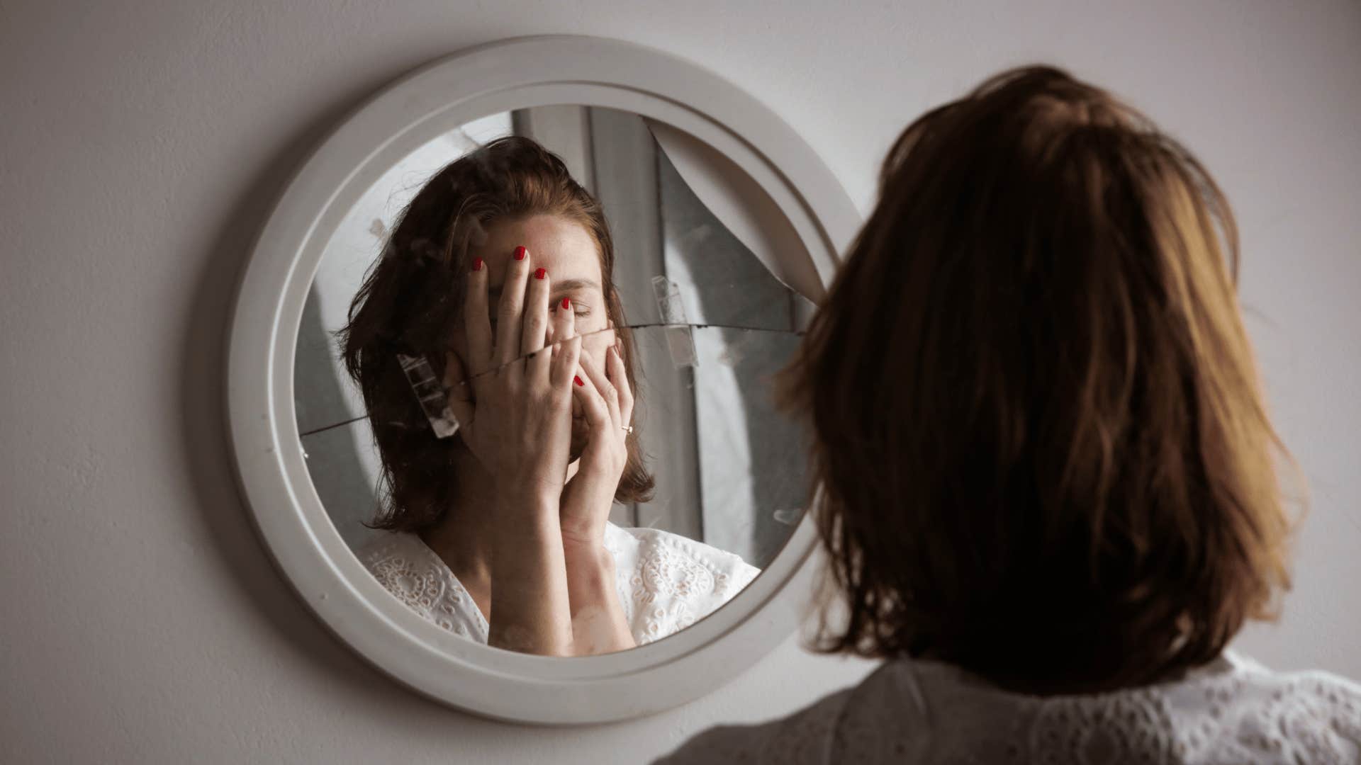 self-conscious woman looking in broken mirror