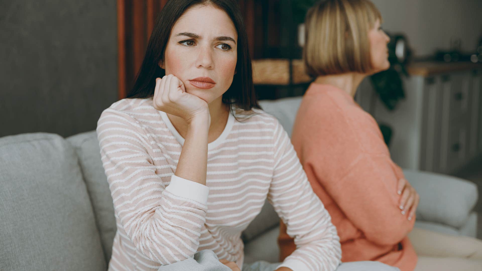 upset adult woman sitting next to mother on couch