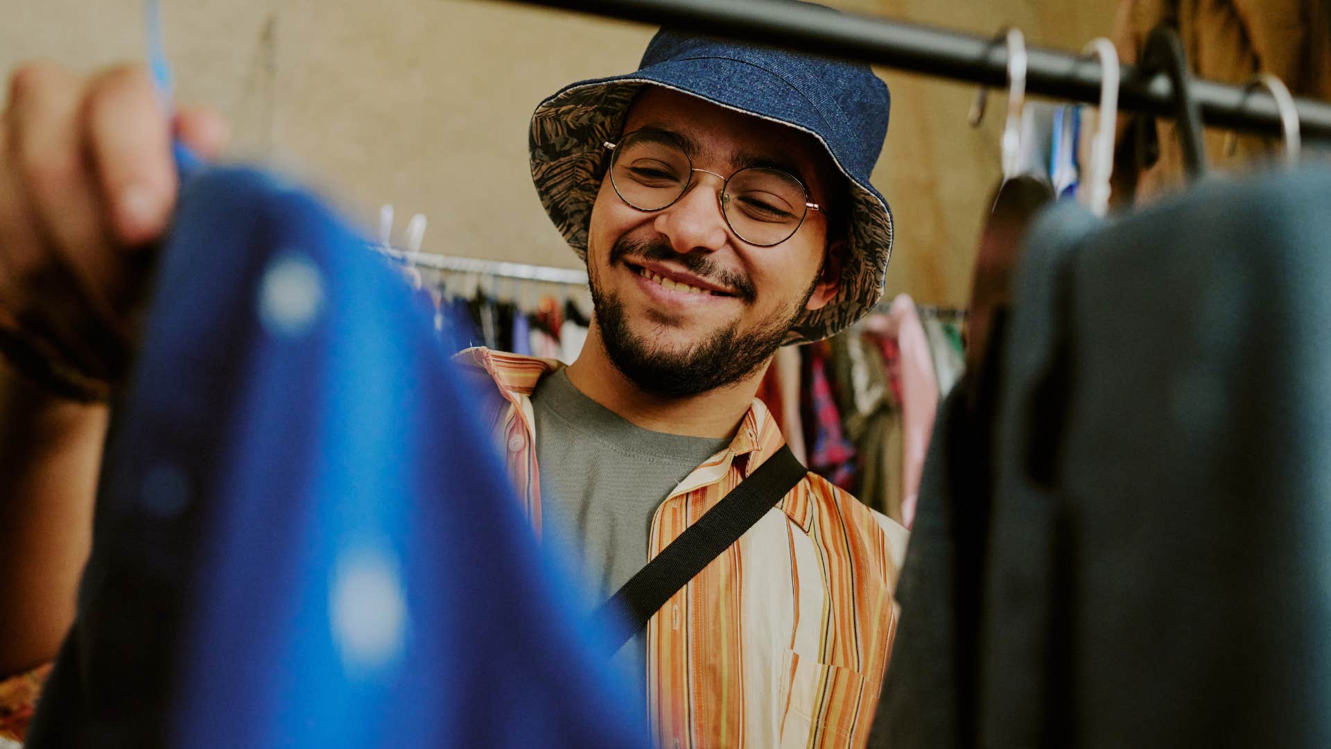 young man smiling while looking at vintage clothes