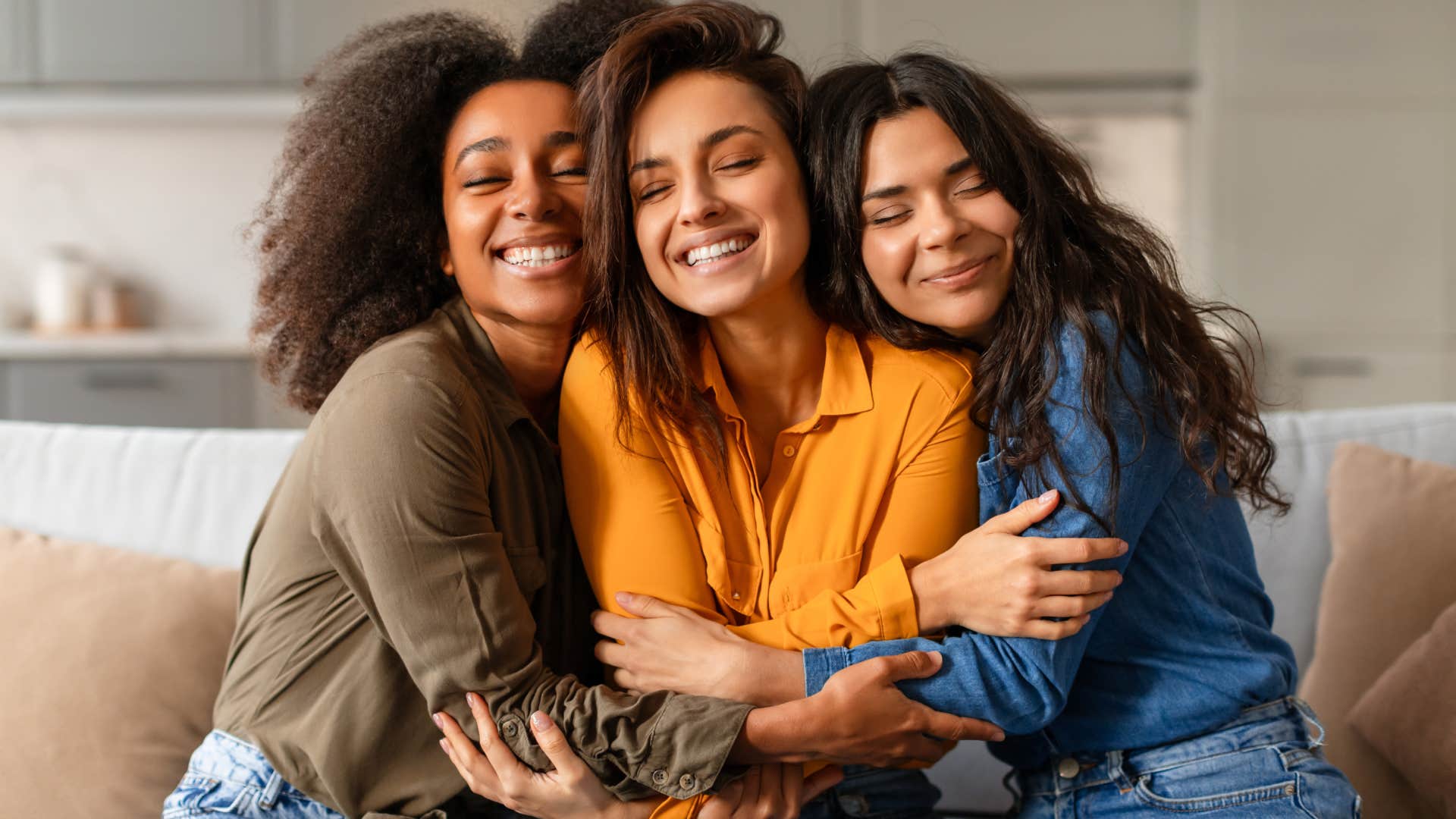 three joyful woman hugging on couch