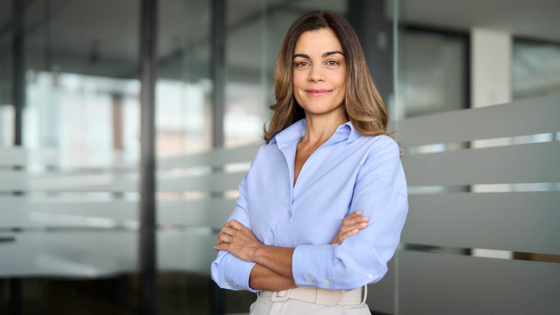 confident smiling businesswoman with arms crossed in office