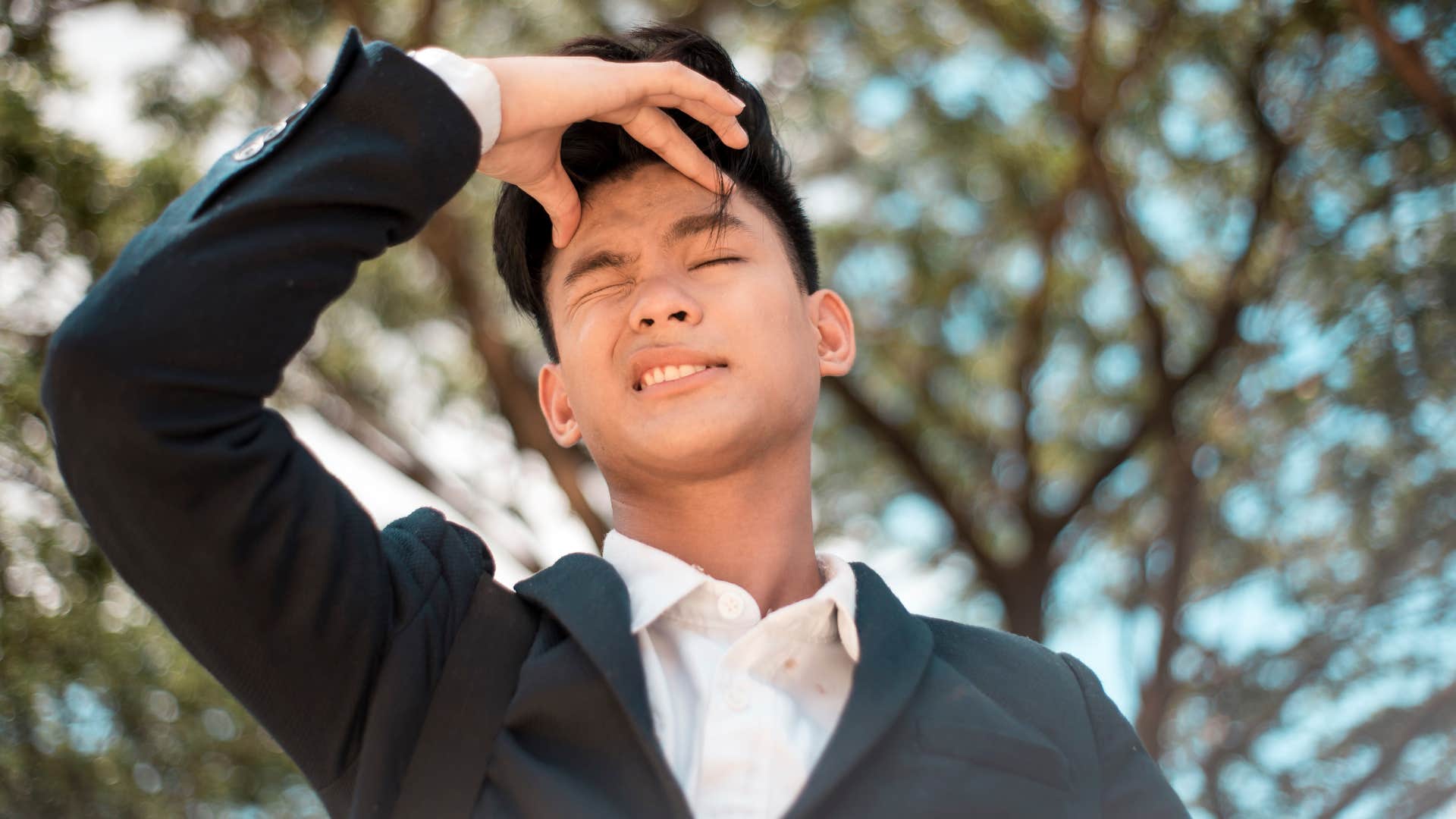 Young man holding his temple outside.