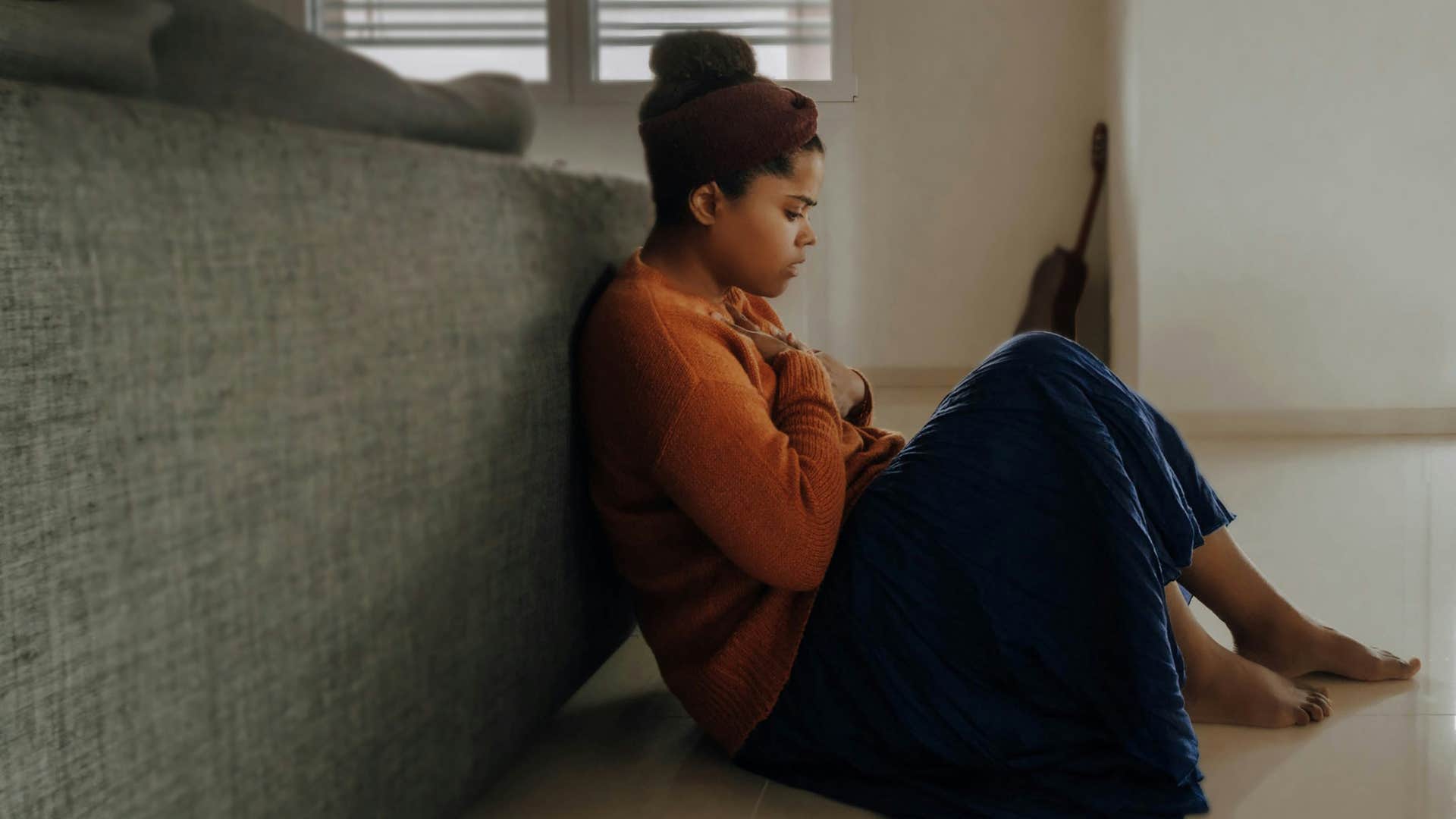 sad woman upset and sitting on the floor behind the couch