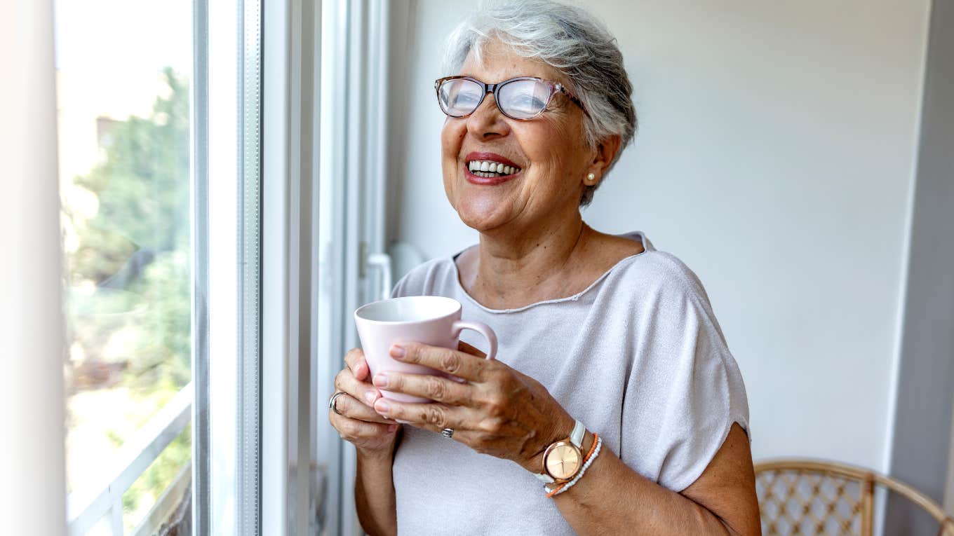 Woman smiling and drinking coffee in front of a window