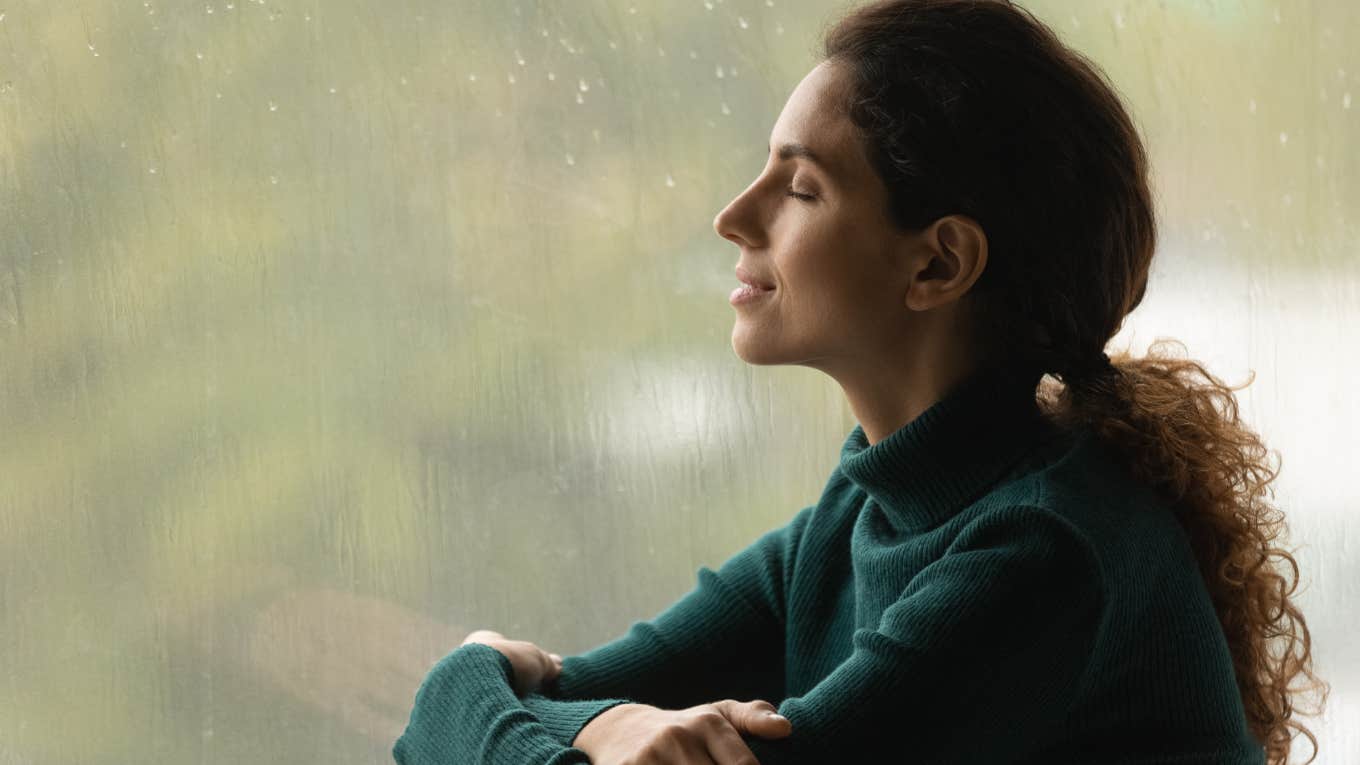 Woman smiling and looking out her window at rain