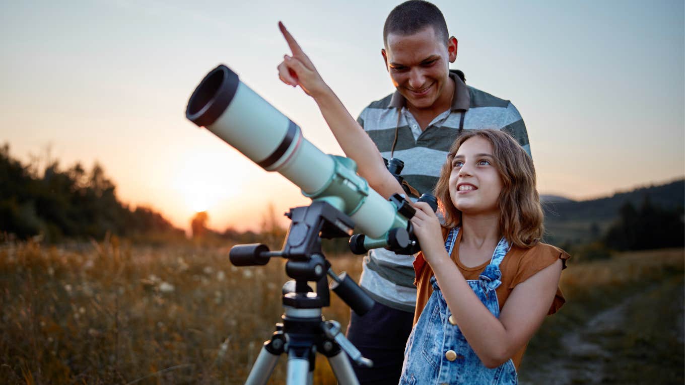 Man smiling and looking through a telescope with his daughter