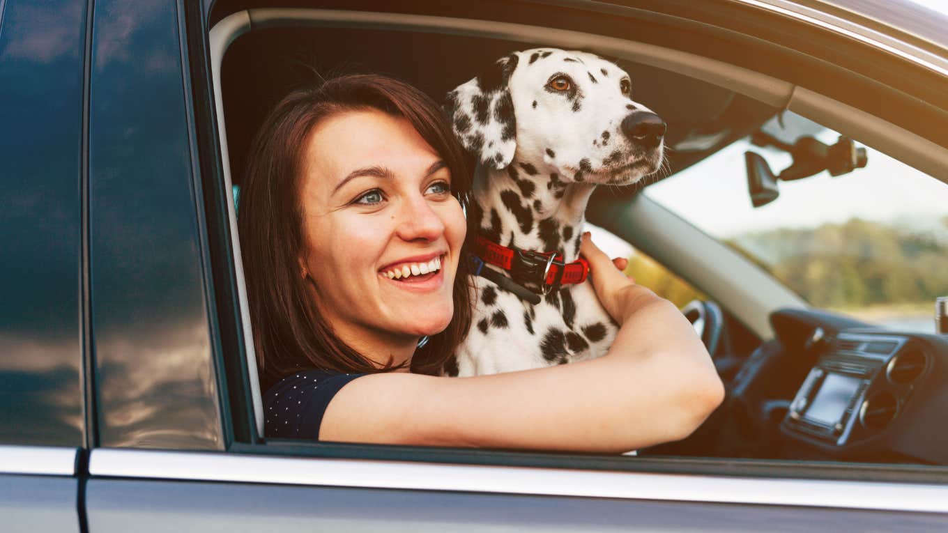 Woman smiling and watching a sunset with her dog from the car