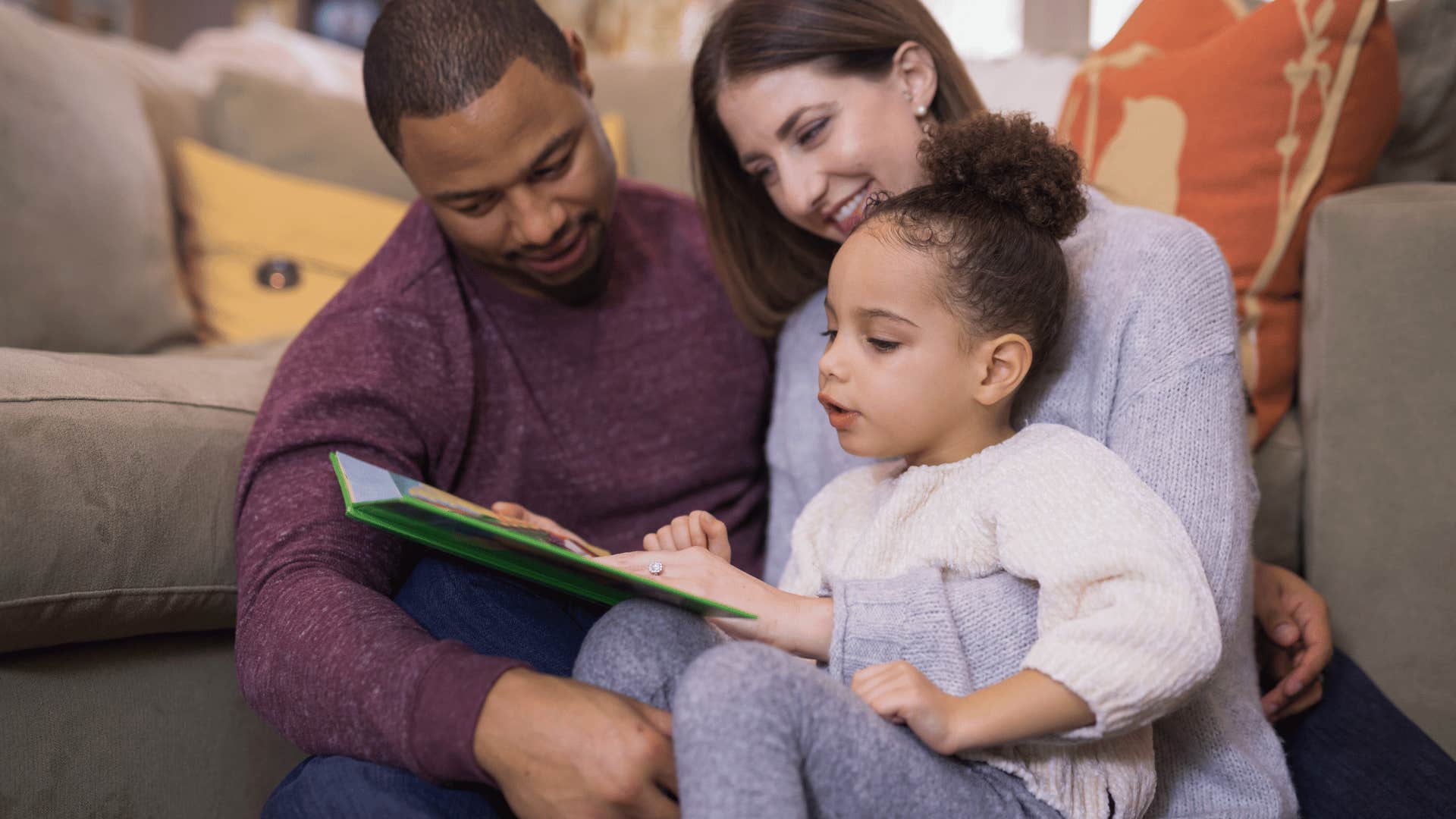 parents reading a book with their daughter