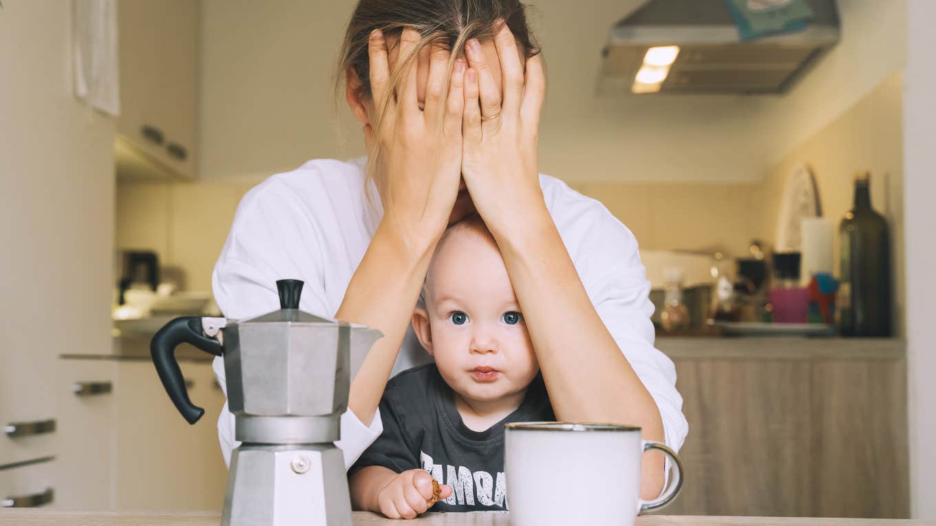 Exhausted woman with baby is sitting with coffee in kitchen