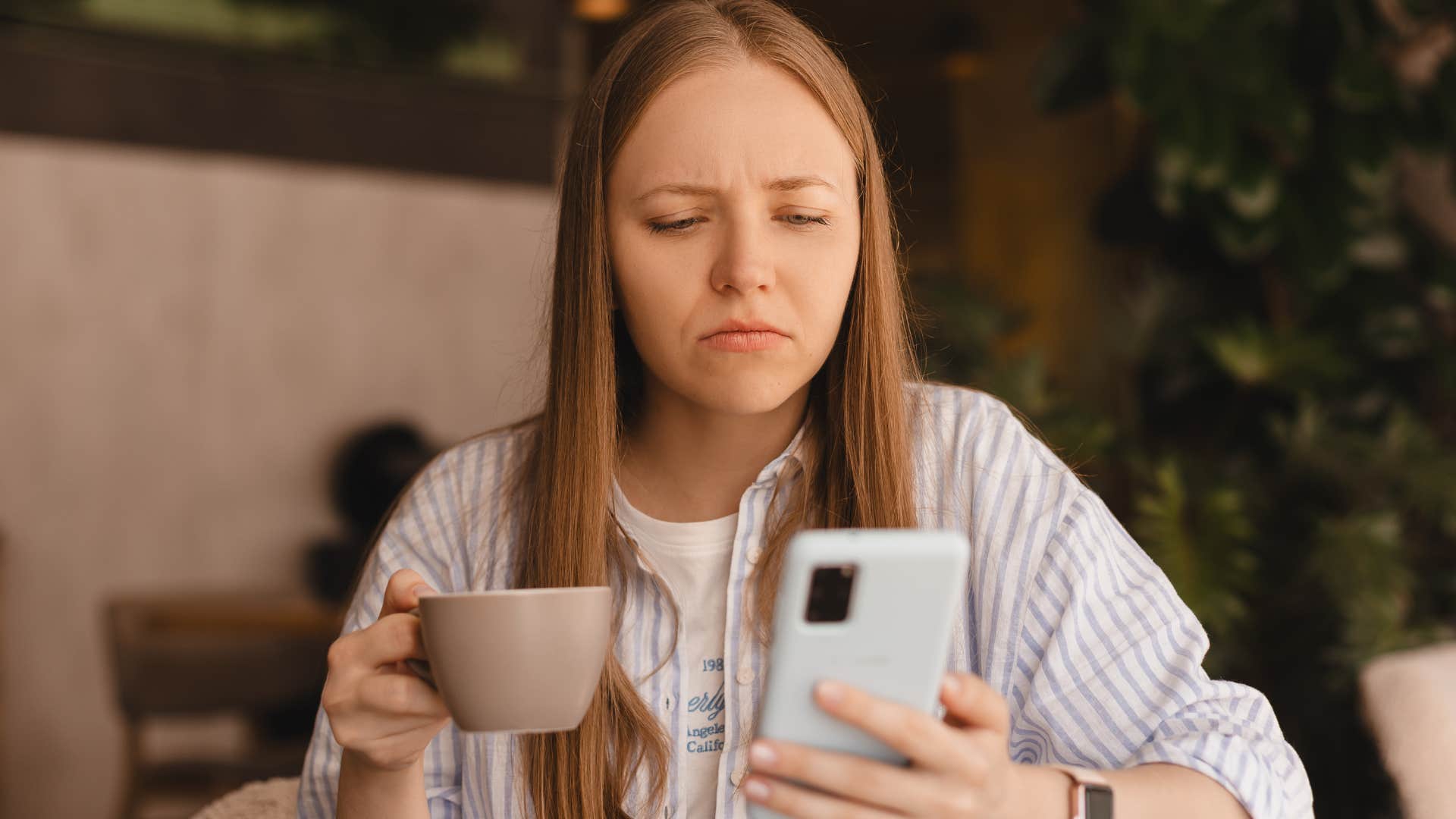 confused young woman drinking coffee while on her phone