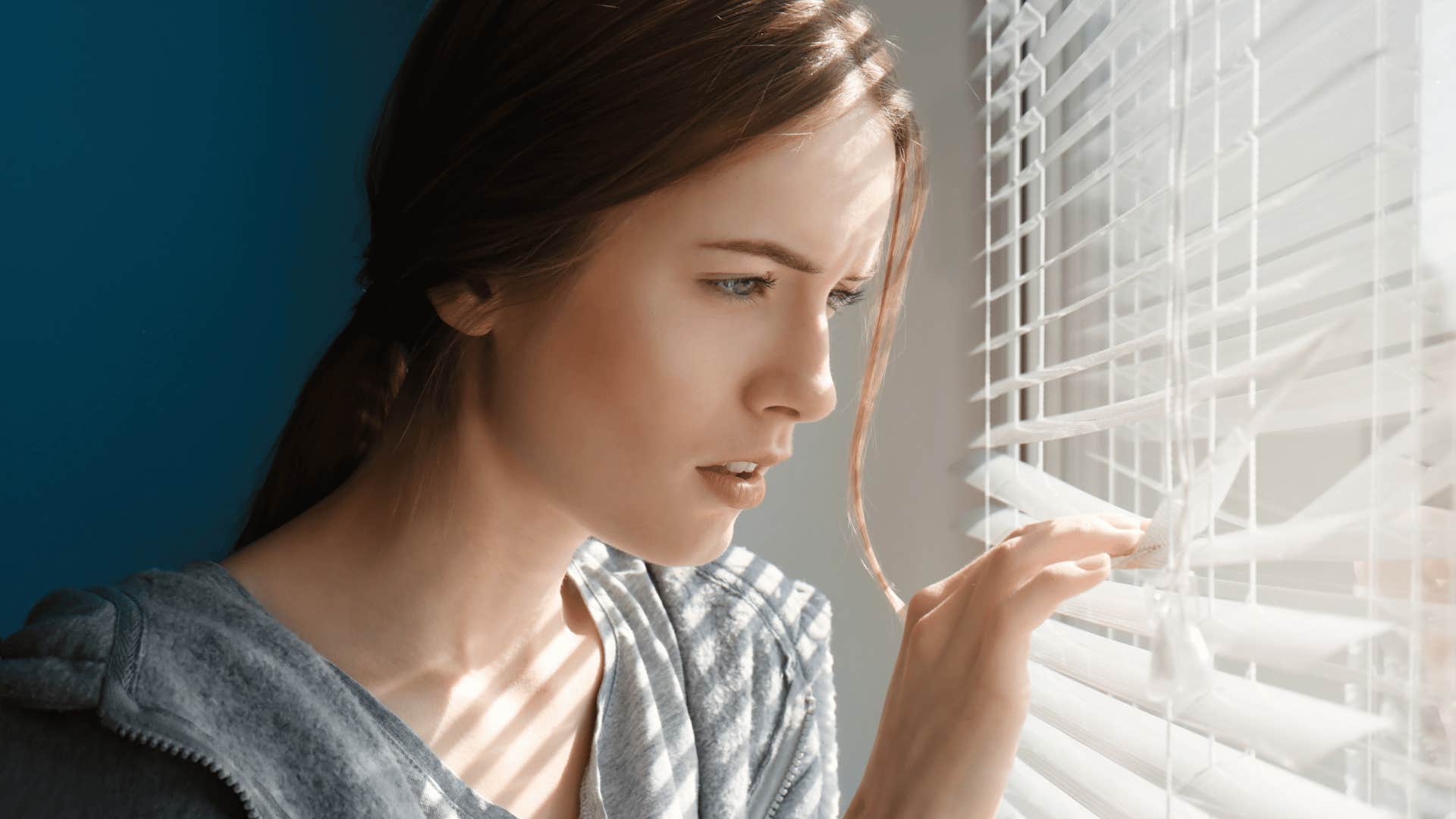 Woman checks outside by looking through window blinds