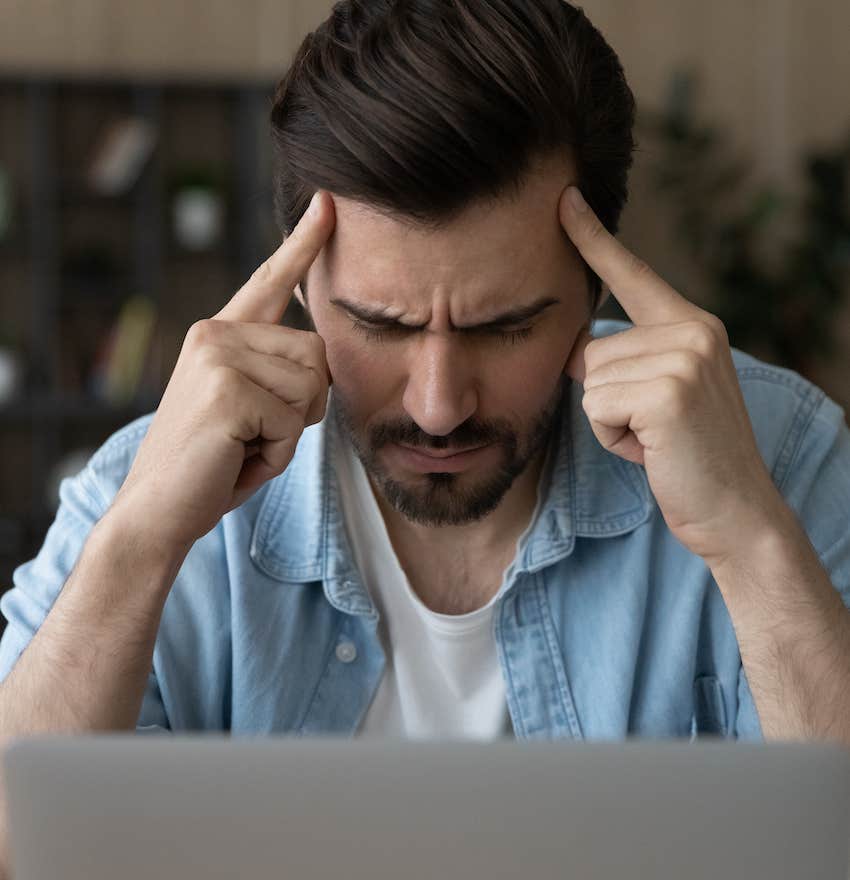 Unavaliable man sits with fingers pressing on his forhead