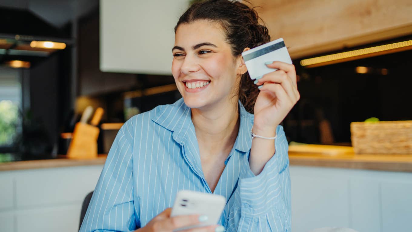 Gen Z woman smiling and holding up a credit card.