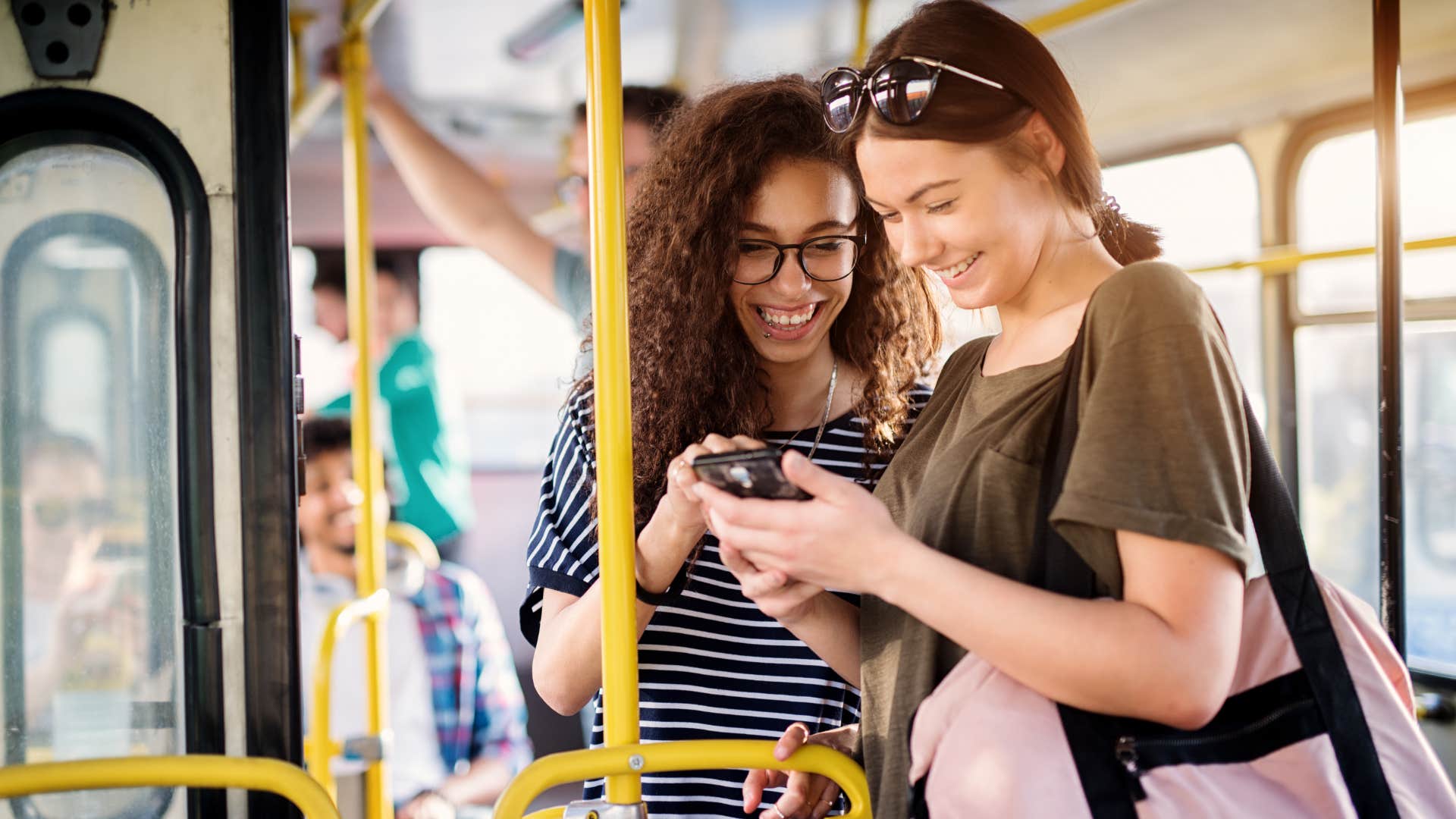 Two Gen Z women smiling and talking on the bus together