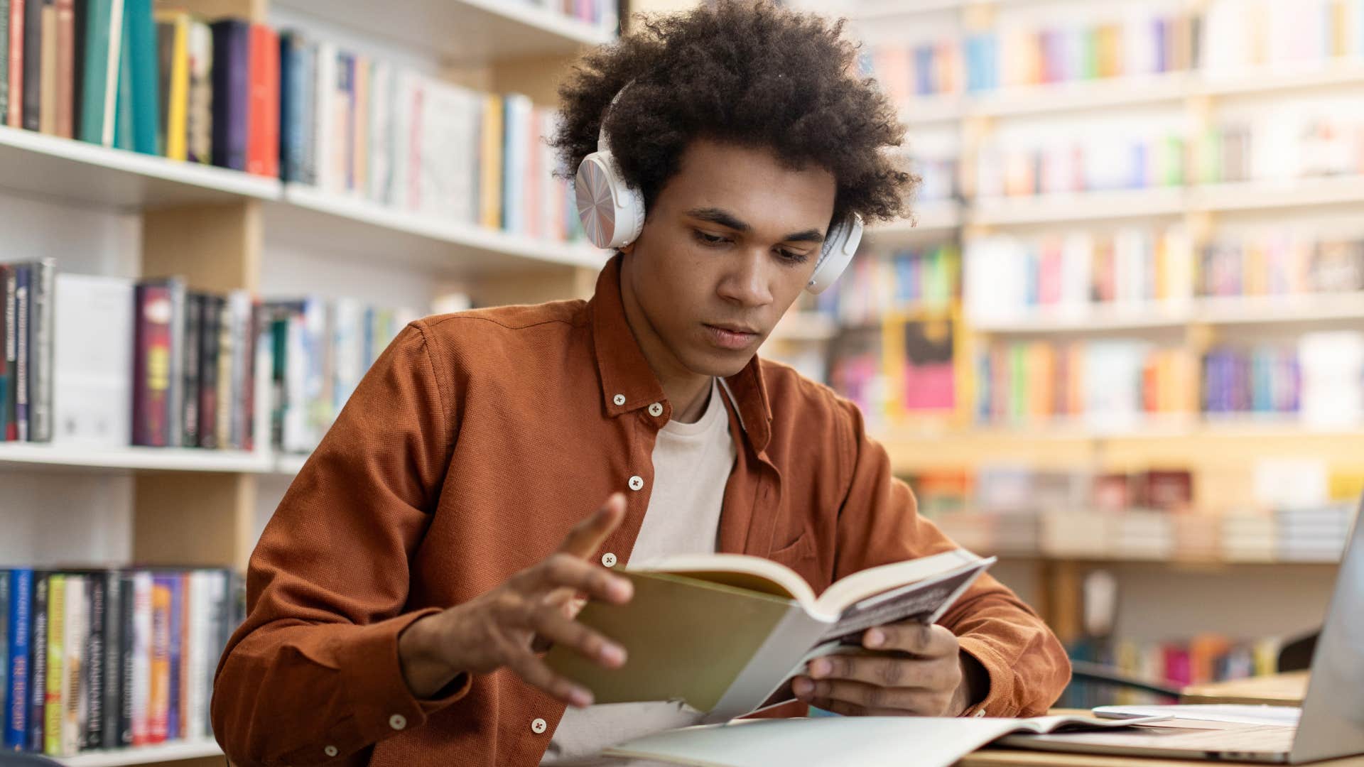 Gen Z man reading a book at a table in a library