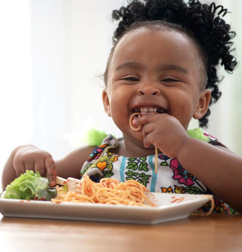 Happy child eats spaghetti with their hands