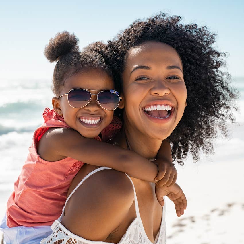 Child rides on mothers back while they play at the beach