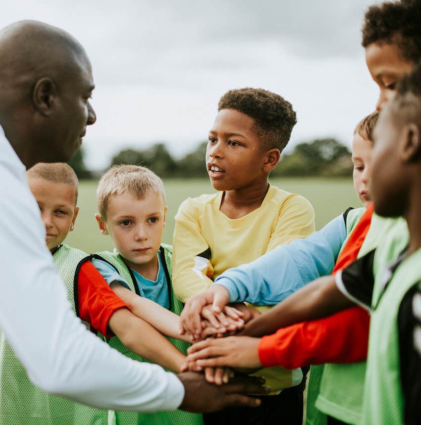 Coach and kids team throw all hands into the center of their circle