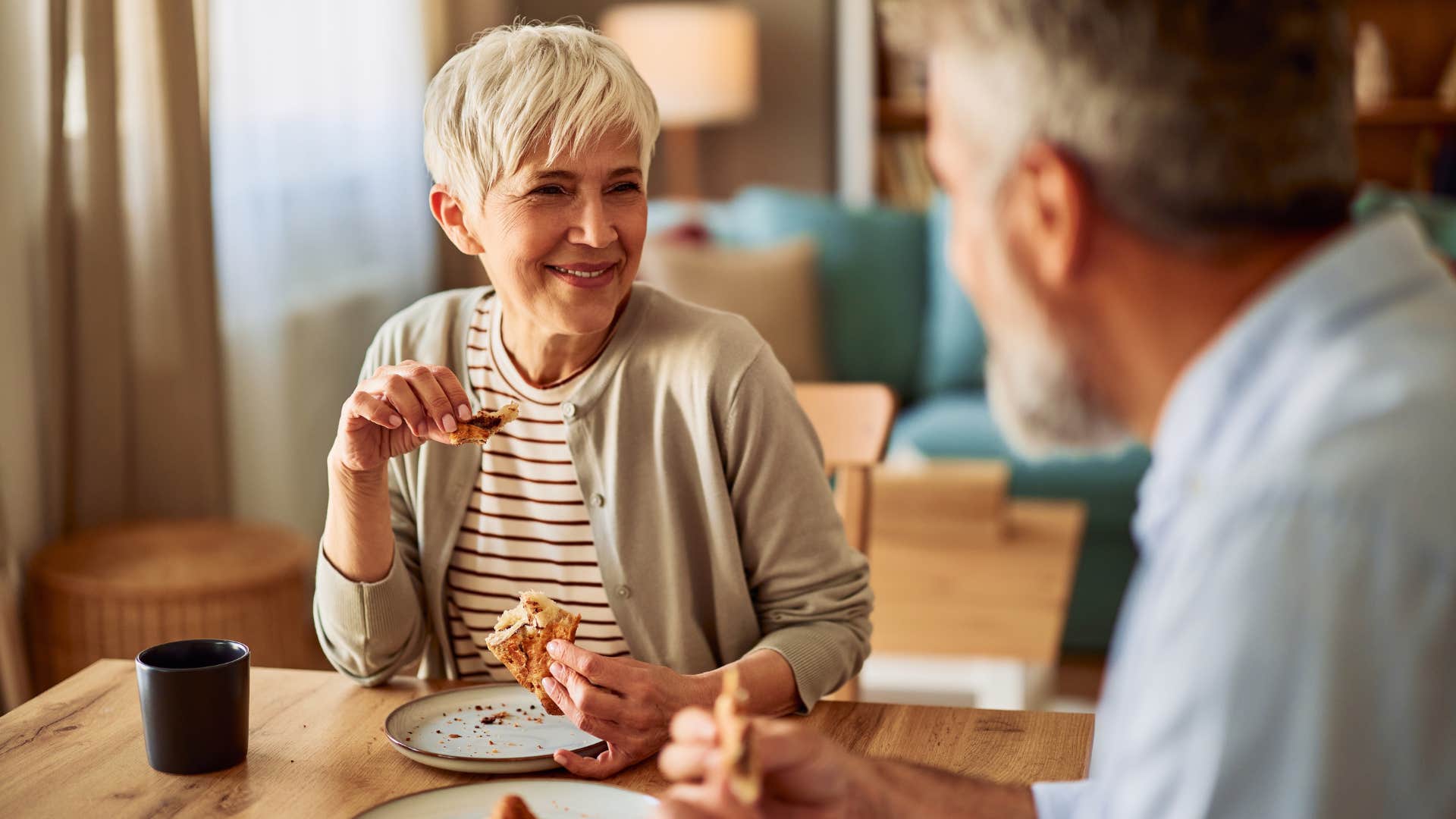 Old woman smiling next to her husband eating an early dinner