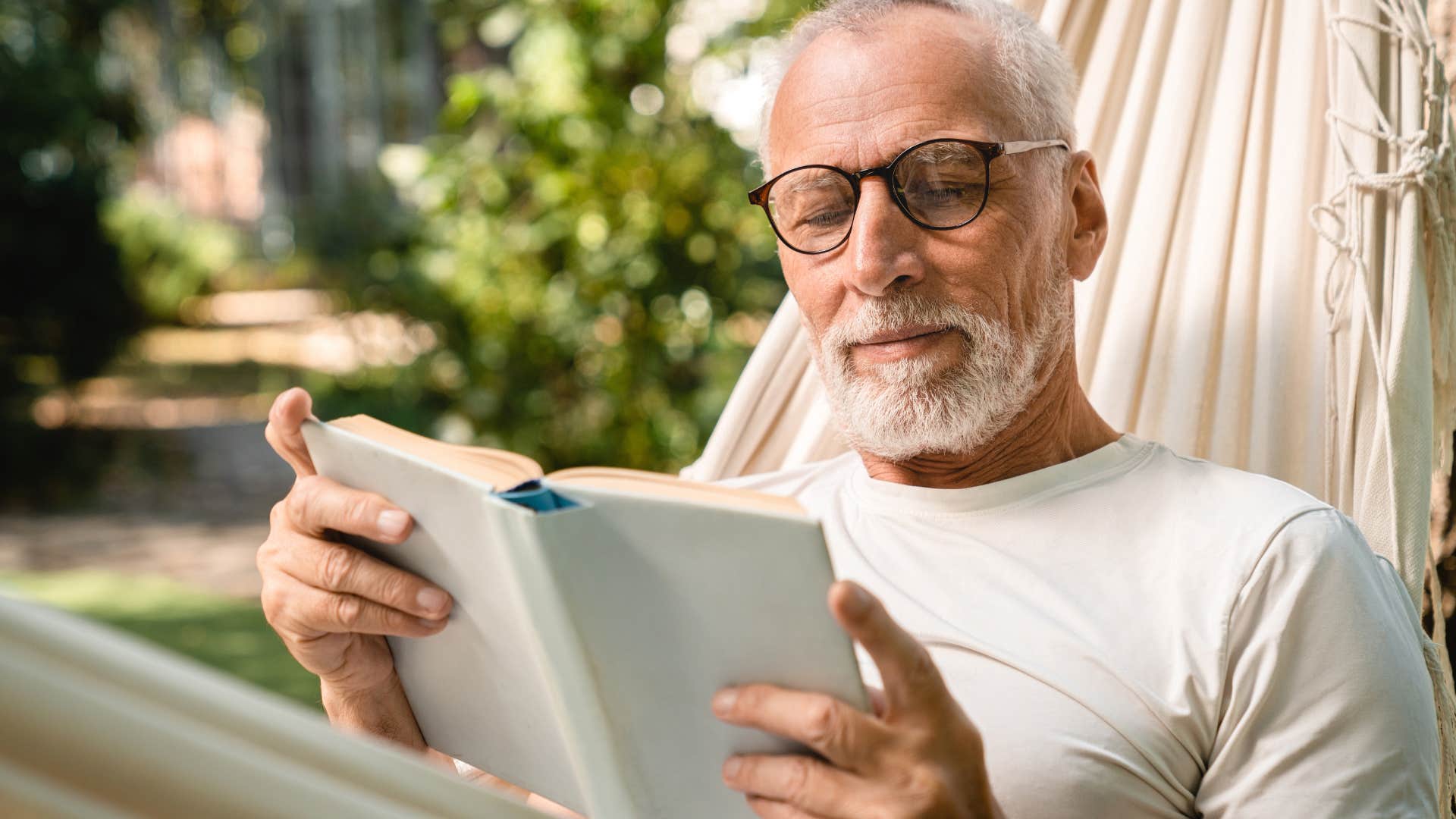 Old man sitting in a hammock reading a book