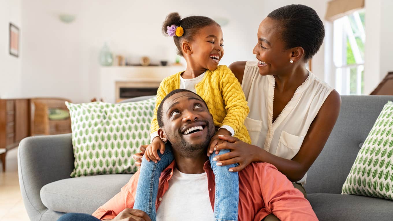 little girl sitting on dad's shoulders smiling at mom