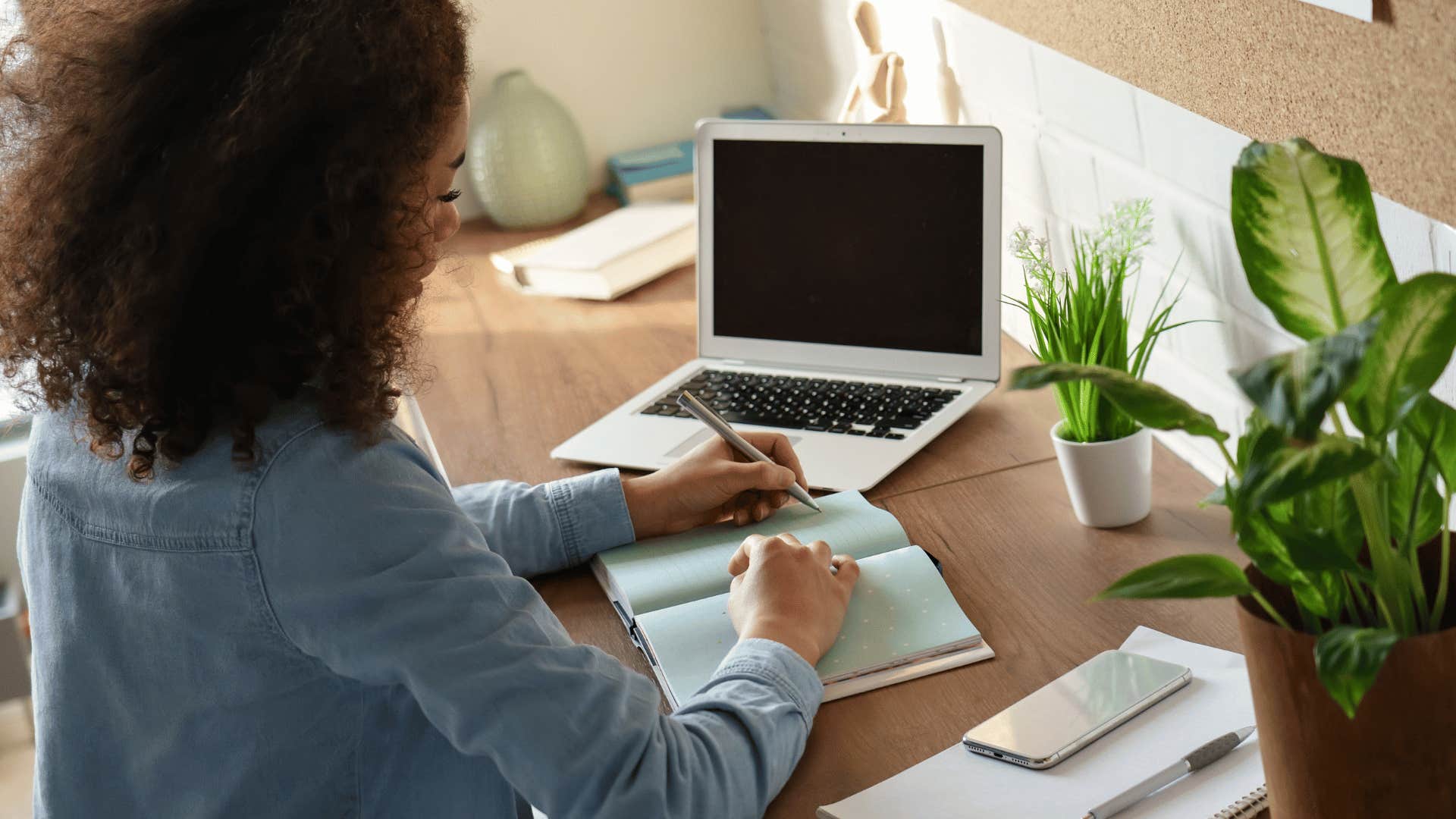 woman writing list in front of laptop