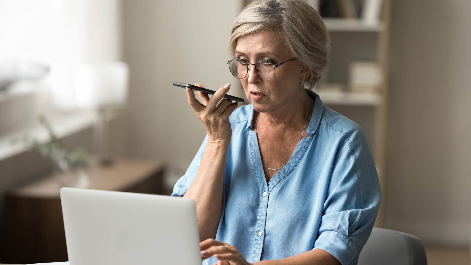 older woman talking into her phone working on computer