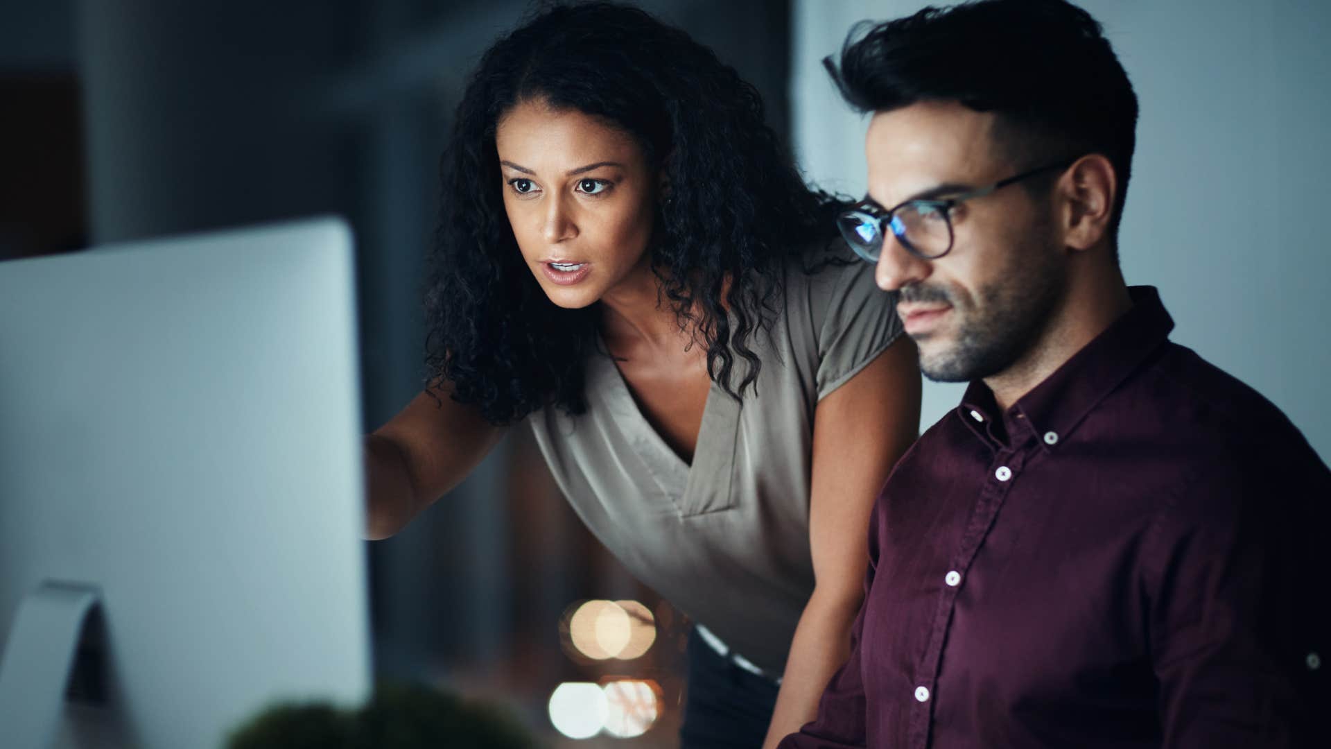 Woman pointing at a man's laptop and talking.